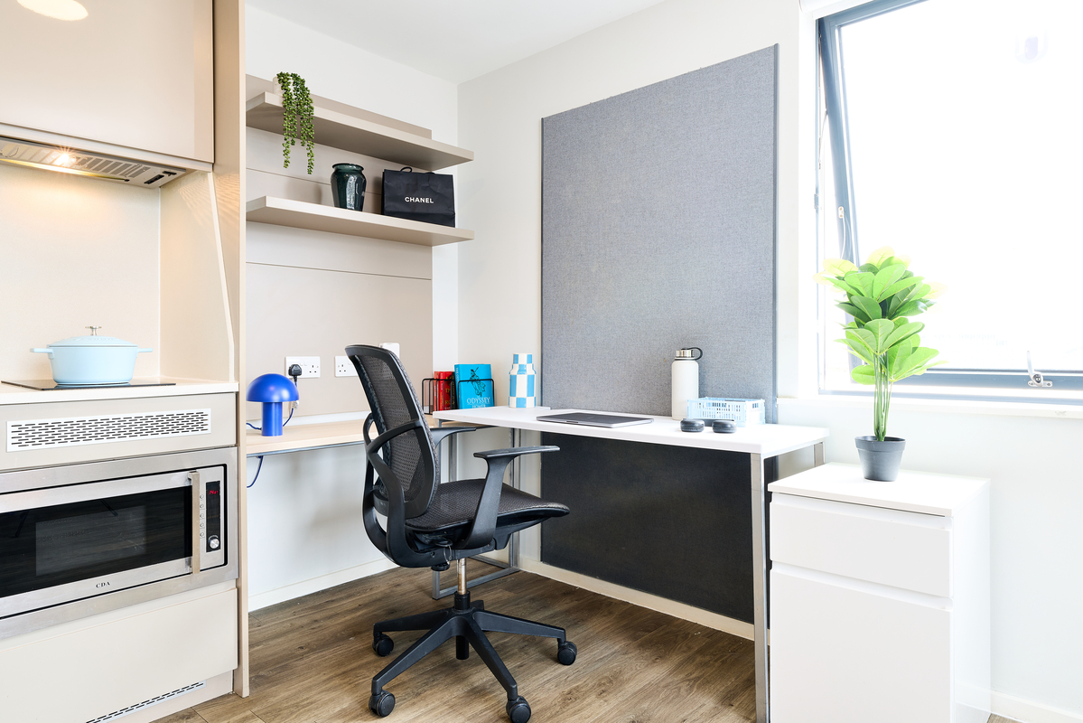 A modern Portland House home office with a black mesh chair at a white desk, shelves with plants and decor, a large window, and a small potted plant on a cabinet. The space is bright and organized with light wood floors.