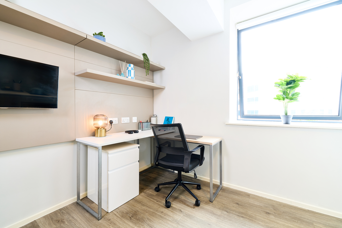 A modern, minimalist Portland House home office with a white desk, black chair, desk lamp, stylish shelves, wall-mounted TV, and a large window with a potted plant that fills the space with natural light.