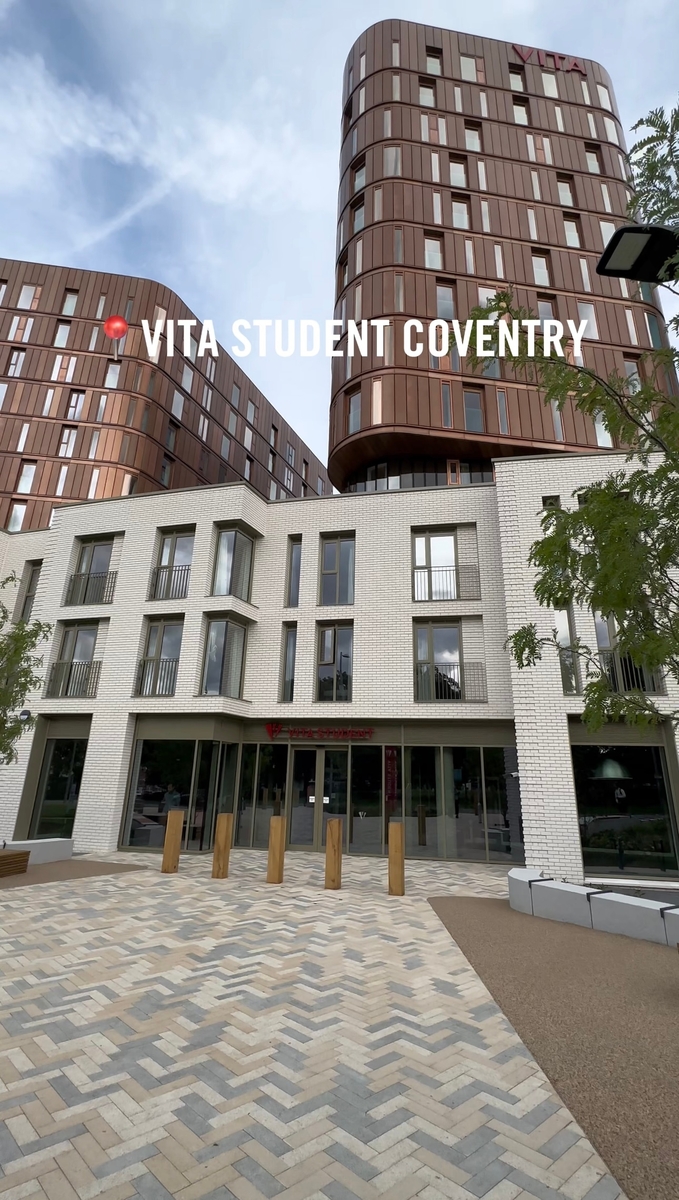 A modern multi-story building with a brown and white facade labeled "VITA STUDENT COVENTRY" offers premium student accommodation in Coventry. The lower portion features large windows and a patterned walkway, while trees and a lamp post beautifully complement the scene in the foreground.