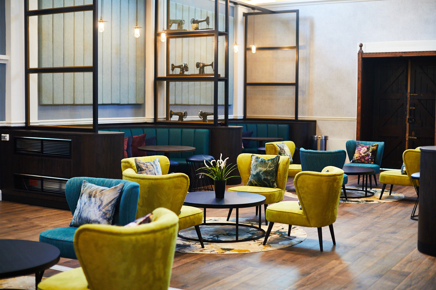 Located on Lawrence Street, this modern cafe boasts a vibrant interior with yellow and teal chairs surrounding circular tables. Decorative vintage sewing machines on shelves add charm, while soft lighting and wooden floors create a cozy atmosphere.