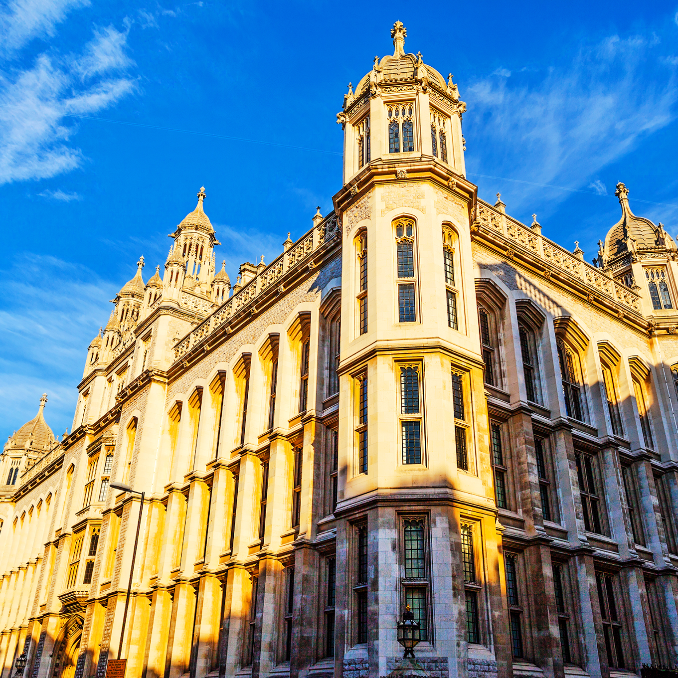 Historic building with intricate architecture under a bright blue sky. The sun casts a warm glow on the stone facade, illuminating ornate windows and domes, creating a striking contrast against the vibrant sky.