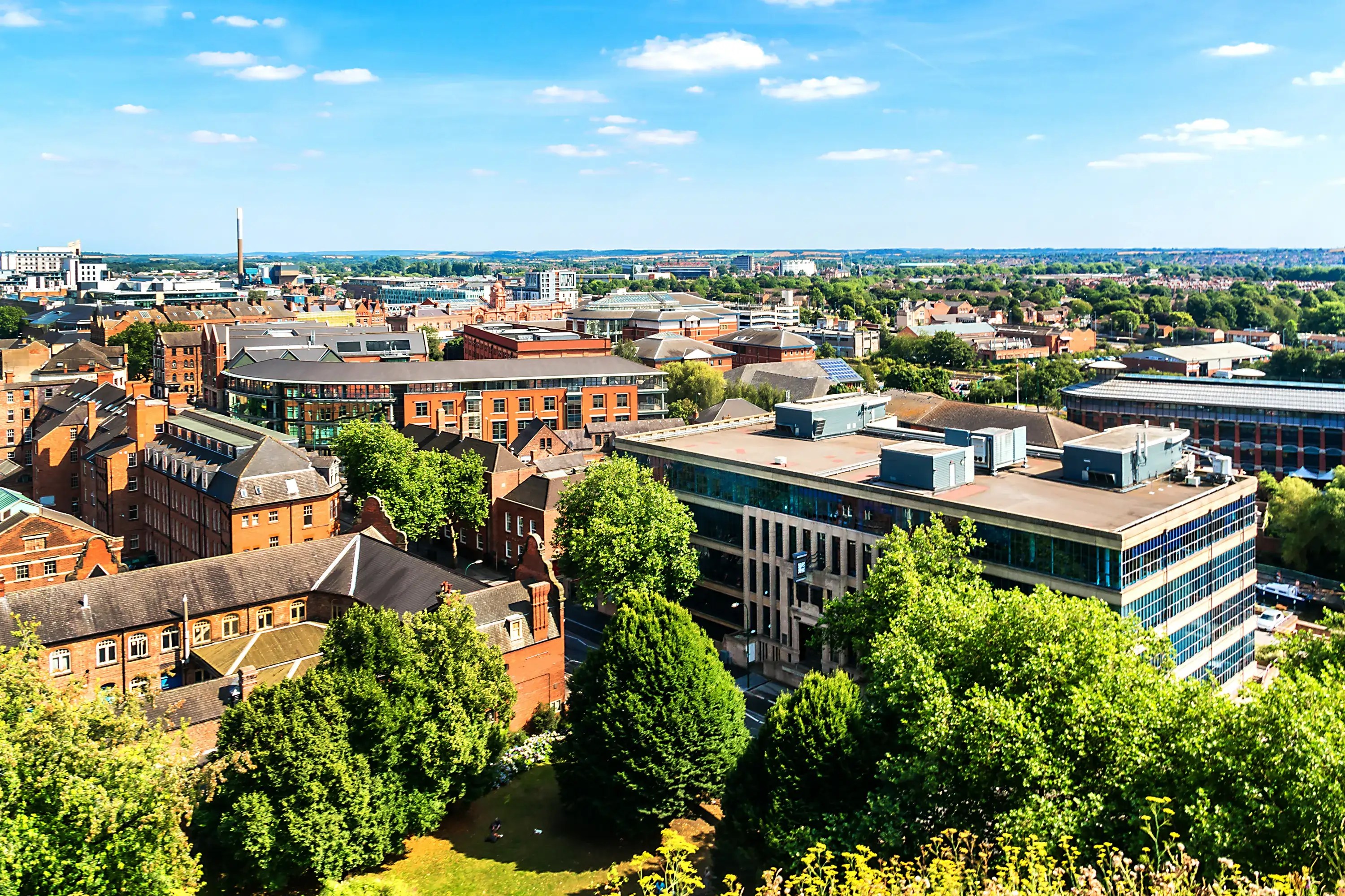 A panoramic view of Nottingham with a mix of modern and historic buildings, including student accommodation in Nottingham, surrounded by trees and greenery under a blue sky with scattered clouds.
