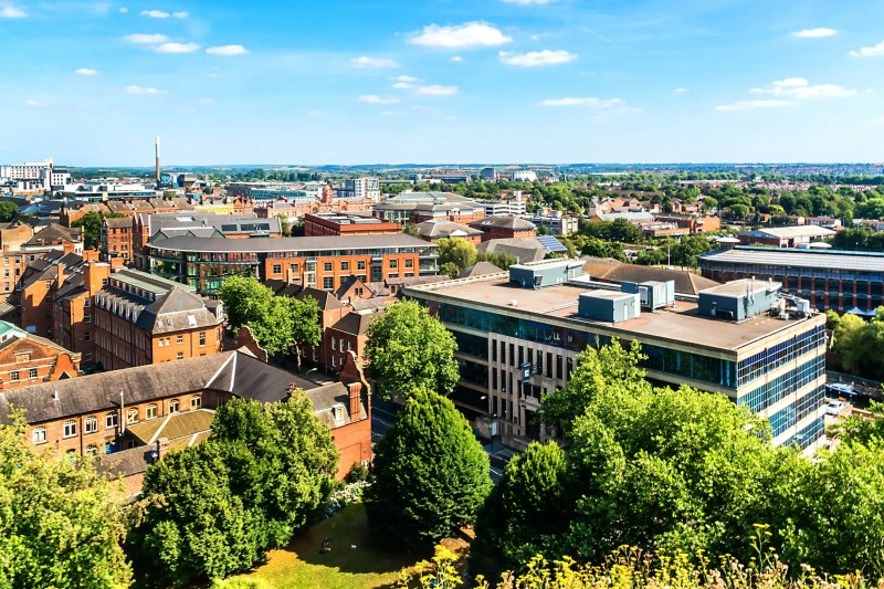 A panoramic view of Nottingham with a mix of modern and historic buildings, including student accommodation in Nottingham, surrounded by trees and greenery under a blue sky with scattered clouds.
