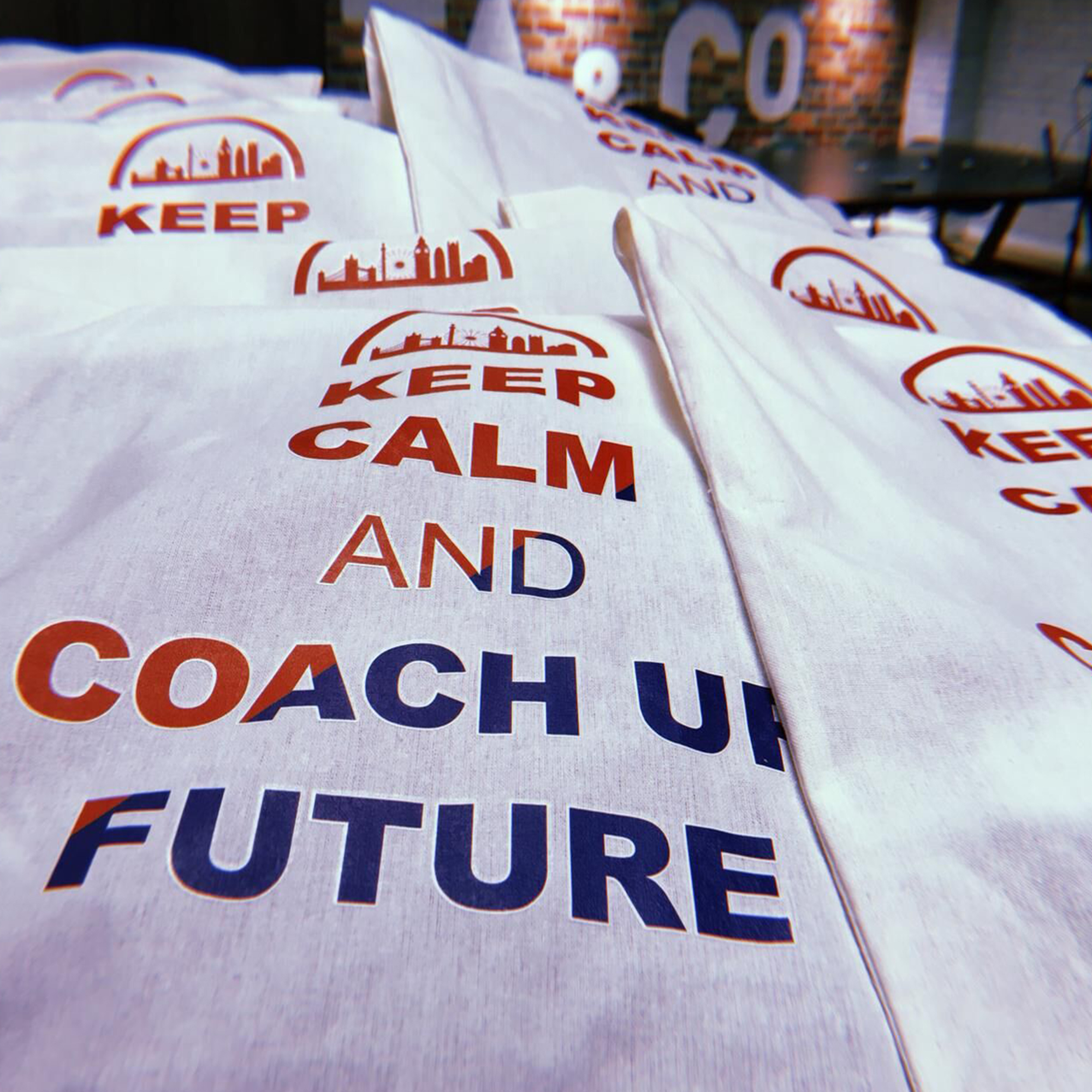 Bags with the text "KEEP CALM AND COACH UP FUTURE" are neatly stacked on a table, featuring silhouettes of buildings above the words. In the backdrop, a brick wall adds character to the setting—a perfect scene for Careers Week 2019 celebrations at Vita Student.