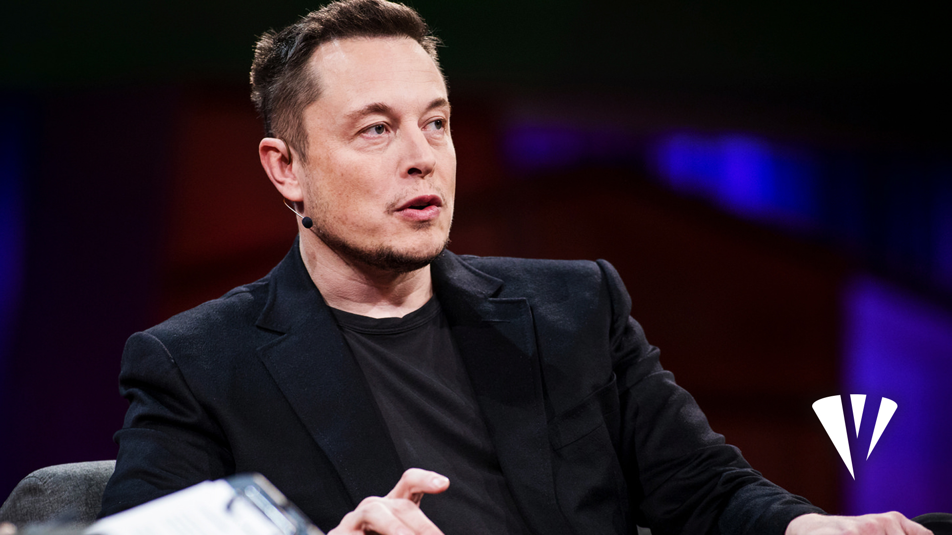 A man in a black suit is seated, gesturing with his hand while discussing start-up resources. The background is blurred with shades of purple and brown, adding an air of mystery. A white logo featuring business tools is visible in the bottom right corner, hinting at innovation and growth.