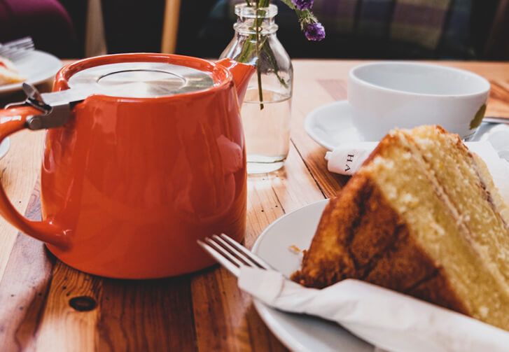 Orange pot of tea and slice of cake.