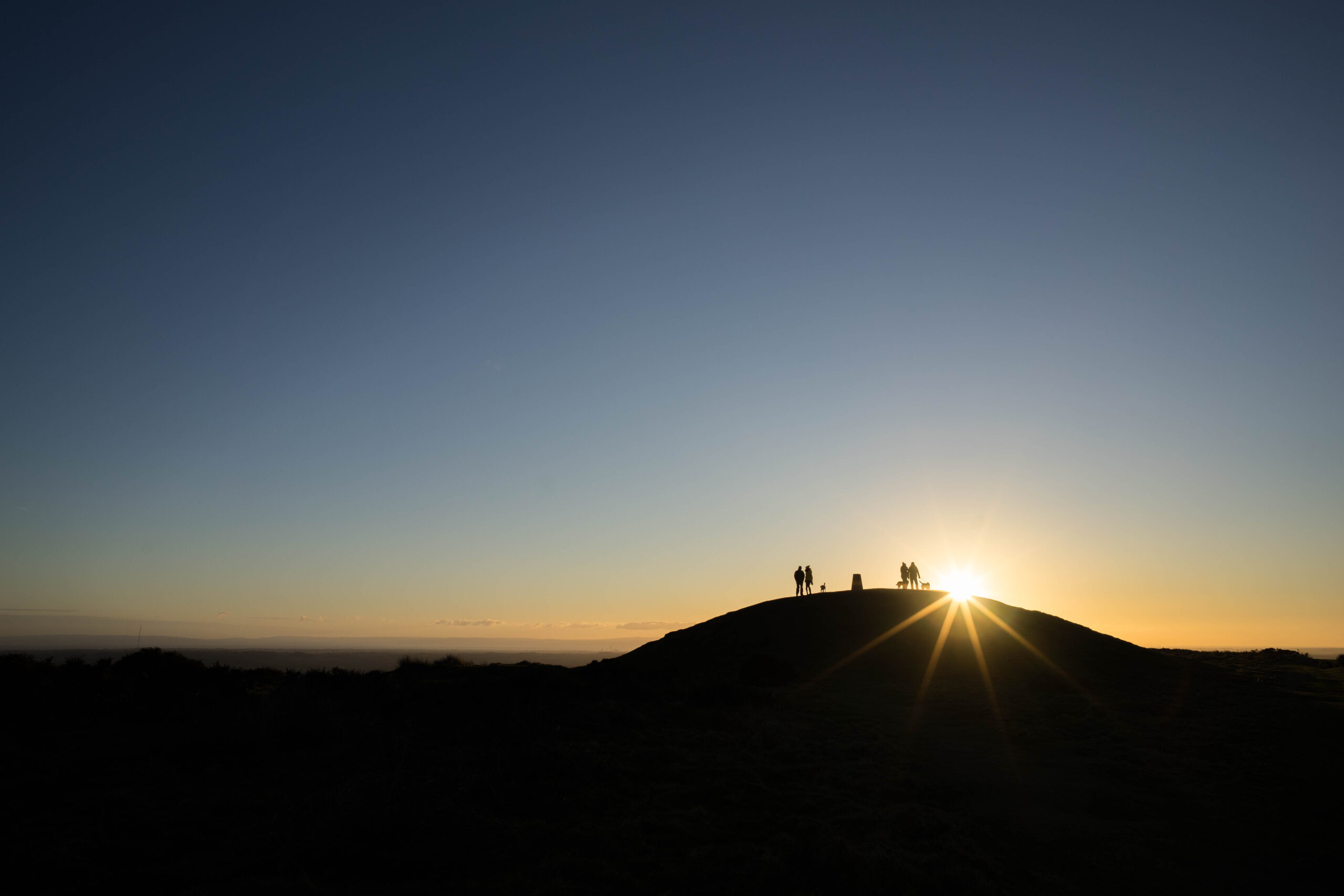 Silhouettes of people standing on top of a hill at sunset.