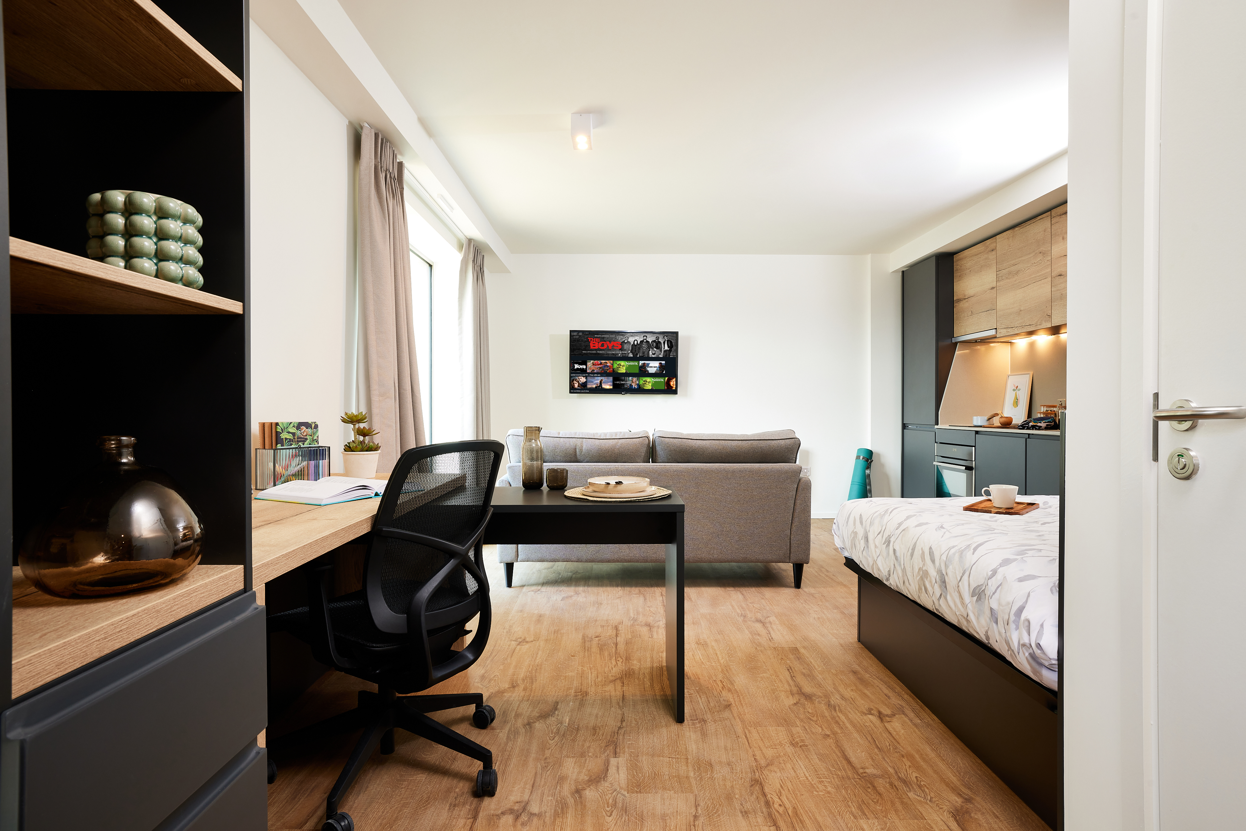 Nestled within the prestigious Copper Towers, this modern studio apartment boasts a wooden floor, offering a cozy bed, a desk with chair, and a sofa facing the TV. Enjoy the kitchen area's wooden cabinets and large windows with light curtains that invite brightness into your airy sanctuary.