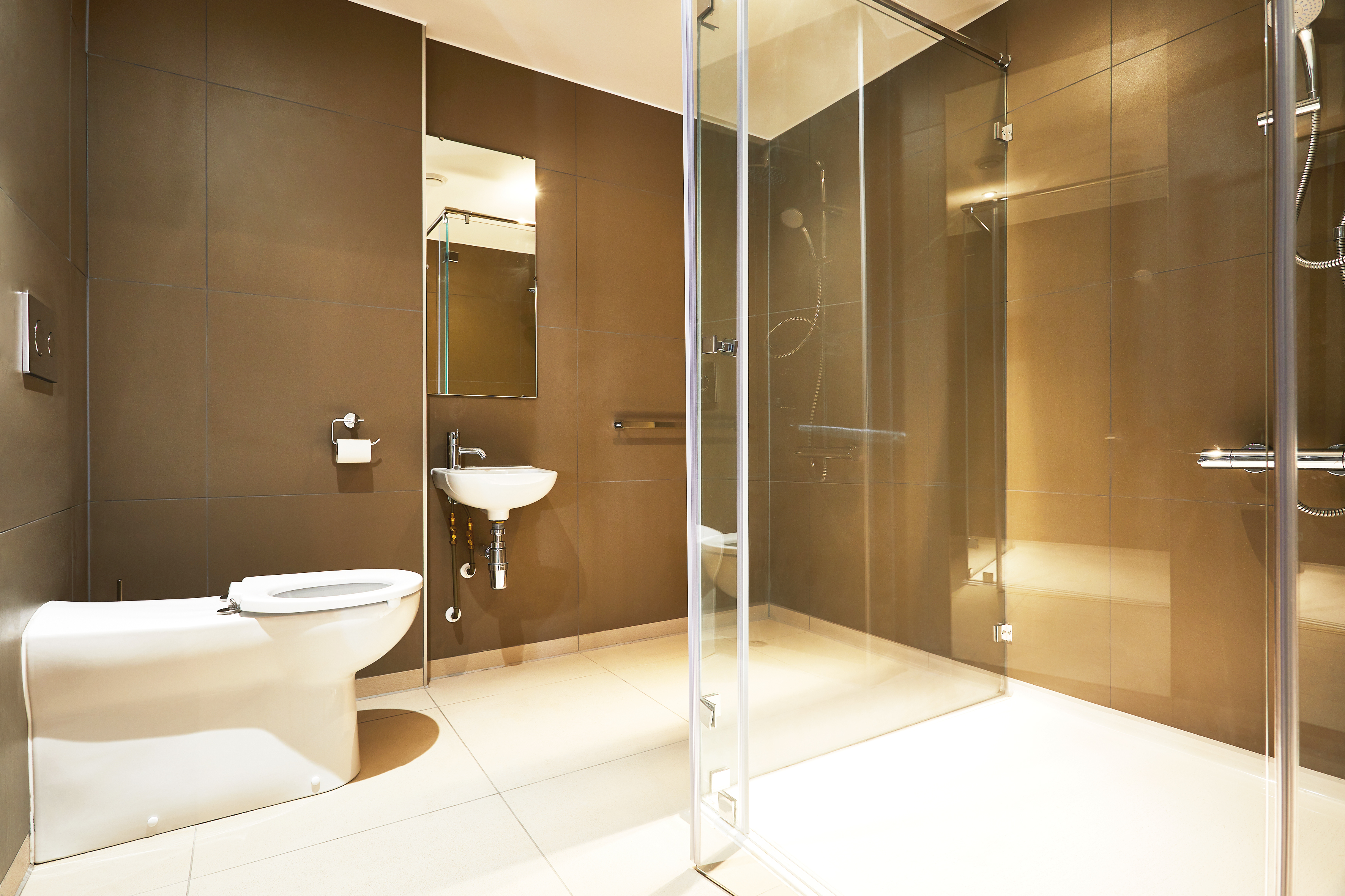 The modern bathroom in Fountainbridge boasts beige tiles and a glass-enclosed shower, complemented by a white toilet and a small white sink with a mirror above. This well-lit space highlights clean lines and minimalist design, creating an oasis of tranquility.