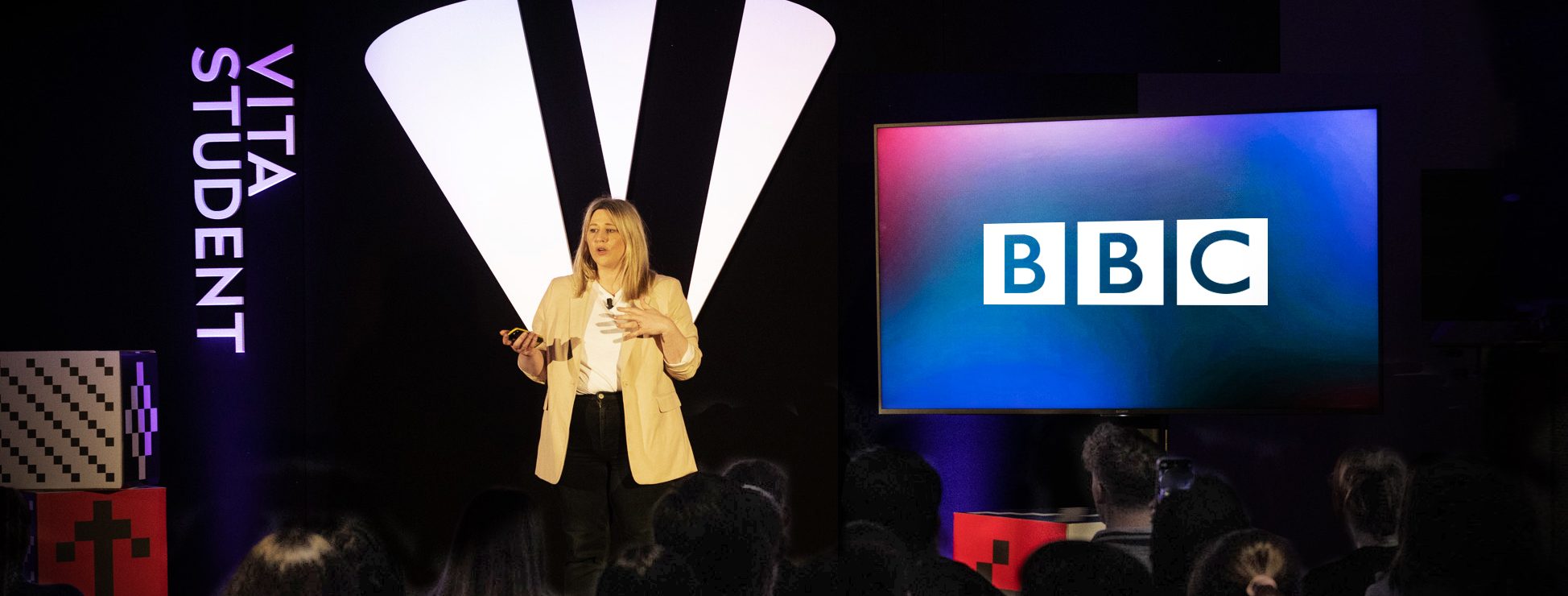 A person stands on a stage delivering career advice at Big Talks 2023. A screen prominently displays the BBC logo, while the backdrop features "VITA STUDENT." The attentive audience is partially visible in front.