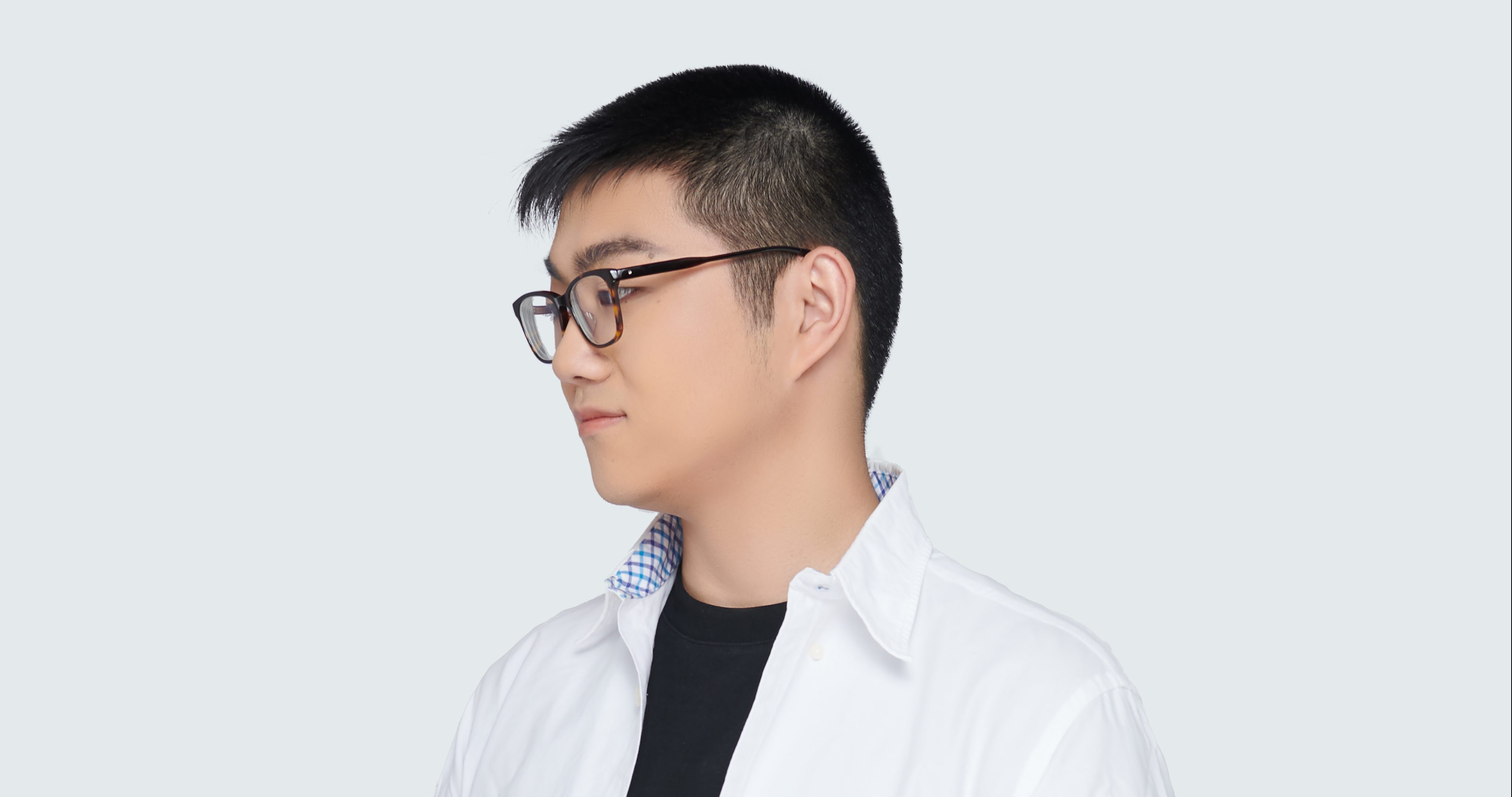 Zihao, with short black hair, glasses, and a white collared shirt over a black t-shirt, gazes to the side against a plain light background, his eyes reflecting the quiet ambition of someone who is always crafting their own story.