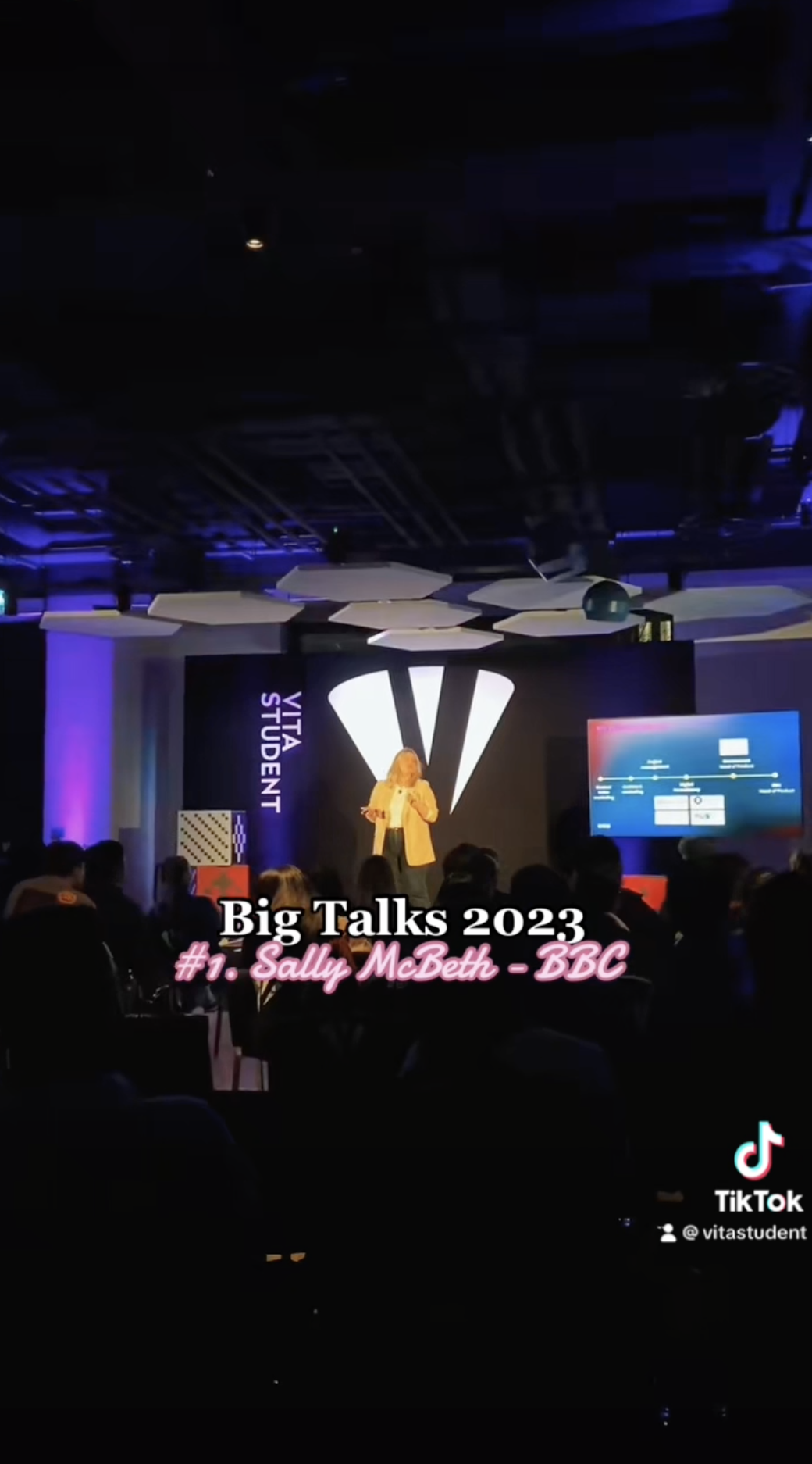 Woman in a light outfit passionately speaking on stage at Big Talks 2023, embodying the theme "Beyond Ambition." A screen and podium accompany her as the audience listens intently. Text on the image reads: "Big Talks 2023" and "#1 - Sally McBeth - BBC.