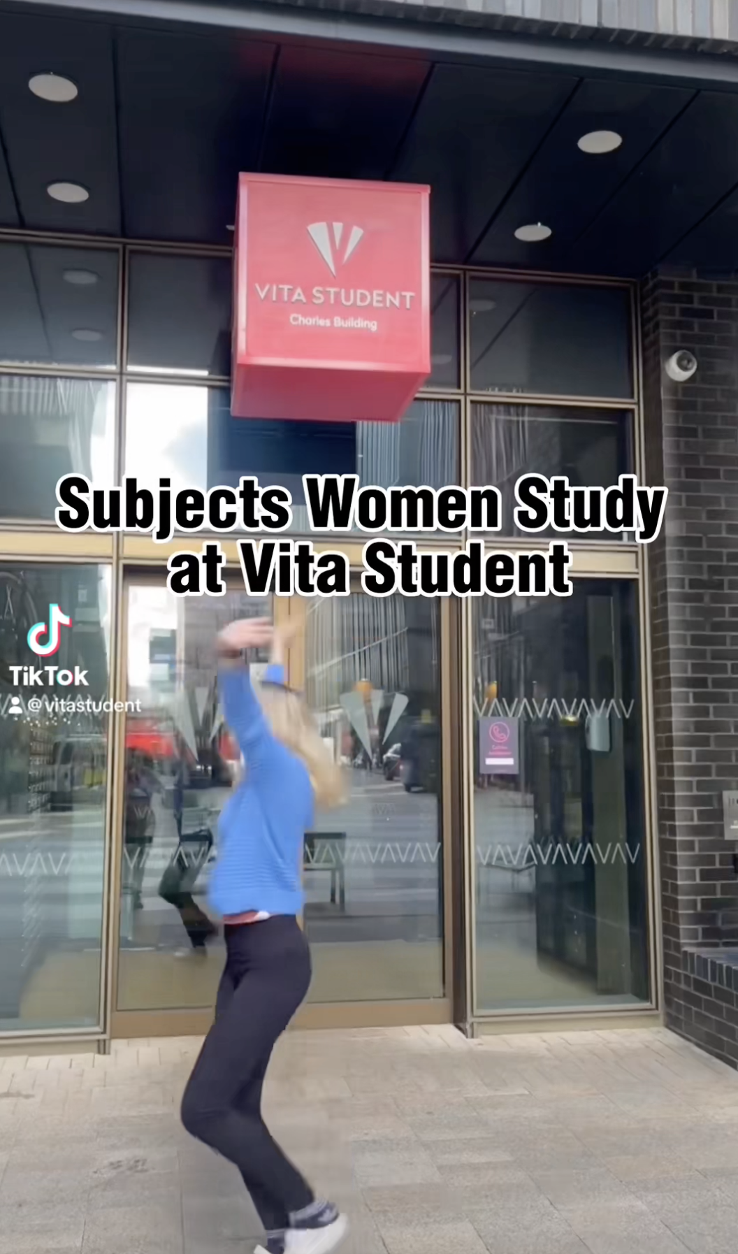 A person in a blue top spins joyfully in front of the Vita Student Chorus Building, embodying the spirit of going "Beyond Ambition." A red sign with the Vita Student logo hangs above the entrance, celebrating the diverse subjects women study at Vita Student.
