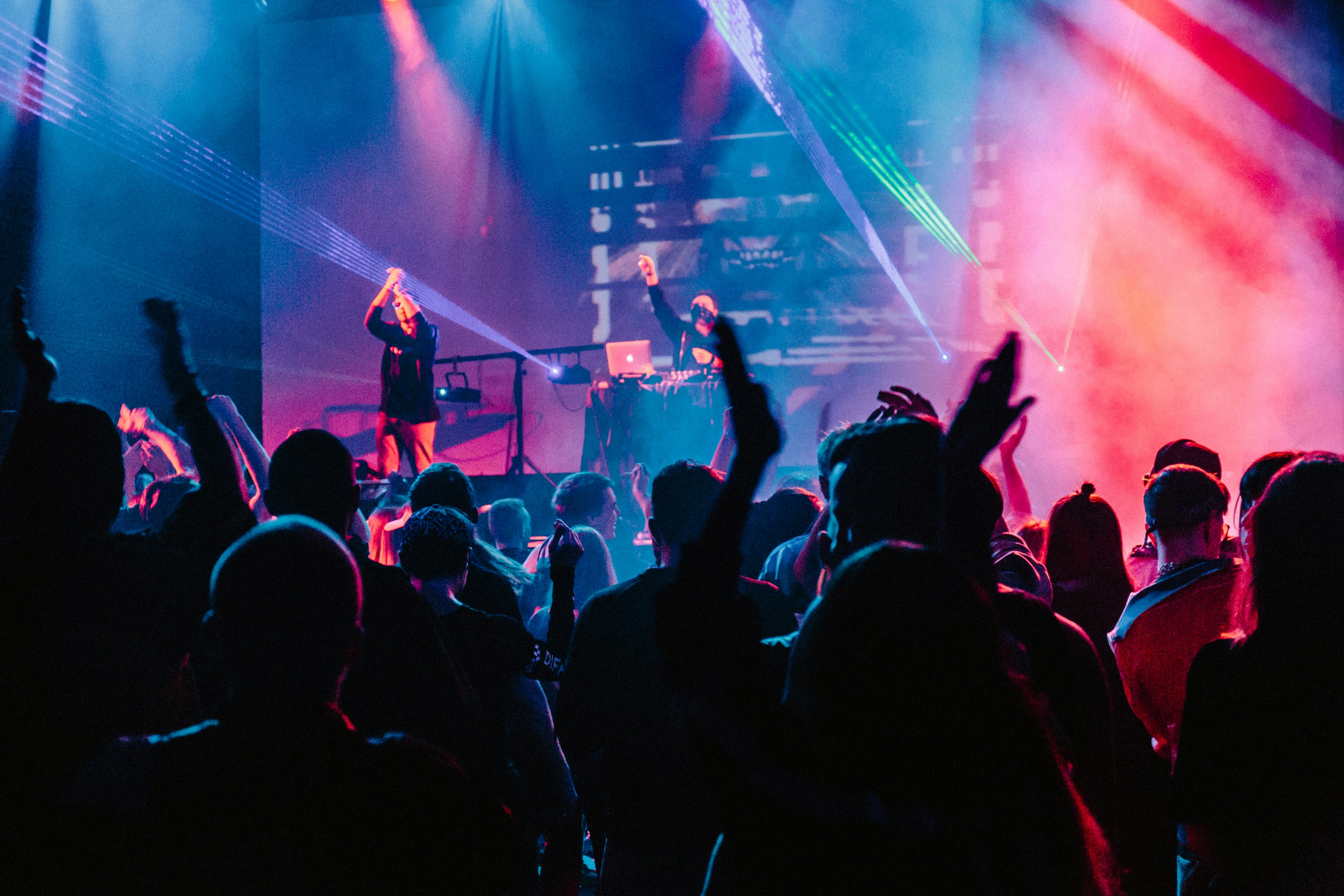 A lively crowd at a Vita Student event in Southampton dances and raises their hands at a concert with colorful stage lights. Two performers—one with a microphone, the other behind a DJ setup—energize the scene as vibrant beams and smoke fill the air.