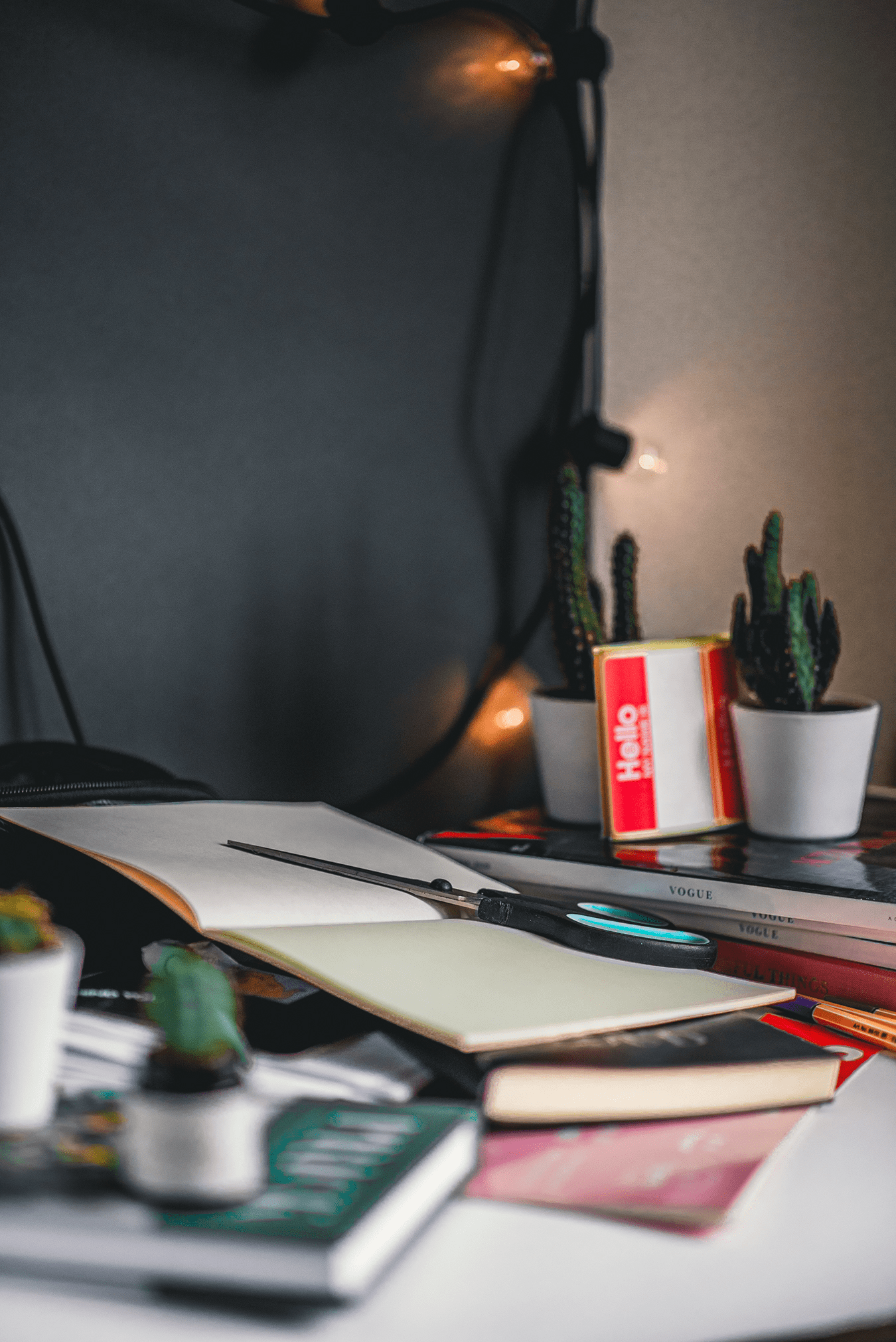 A cluttered desk with important books, an open notebook, pens, and small potted cacti. String lights hang in the background, casting a warm glow over the scene, creating a cozy and creative workspace ambiance—perfect for any University guide in progress.