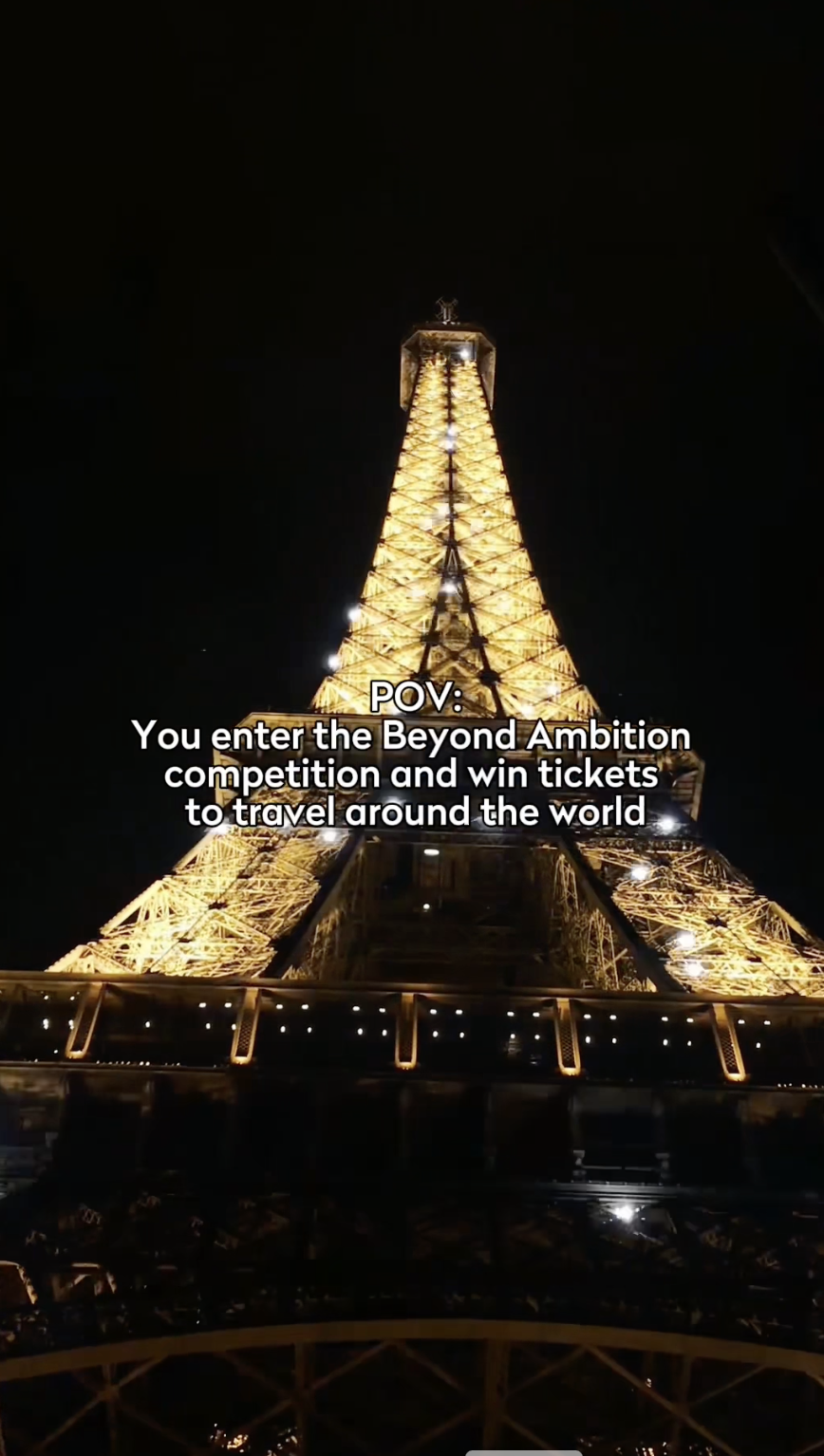 The Eiffel Tower is illuminated at night against a dark sky. Overlaid text reads: "POV: You enter the Beyond Ambition competition, driven by your goals and ambition, and win tickets to travel around the world.