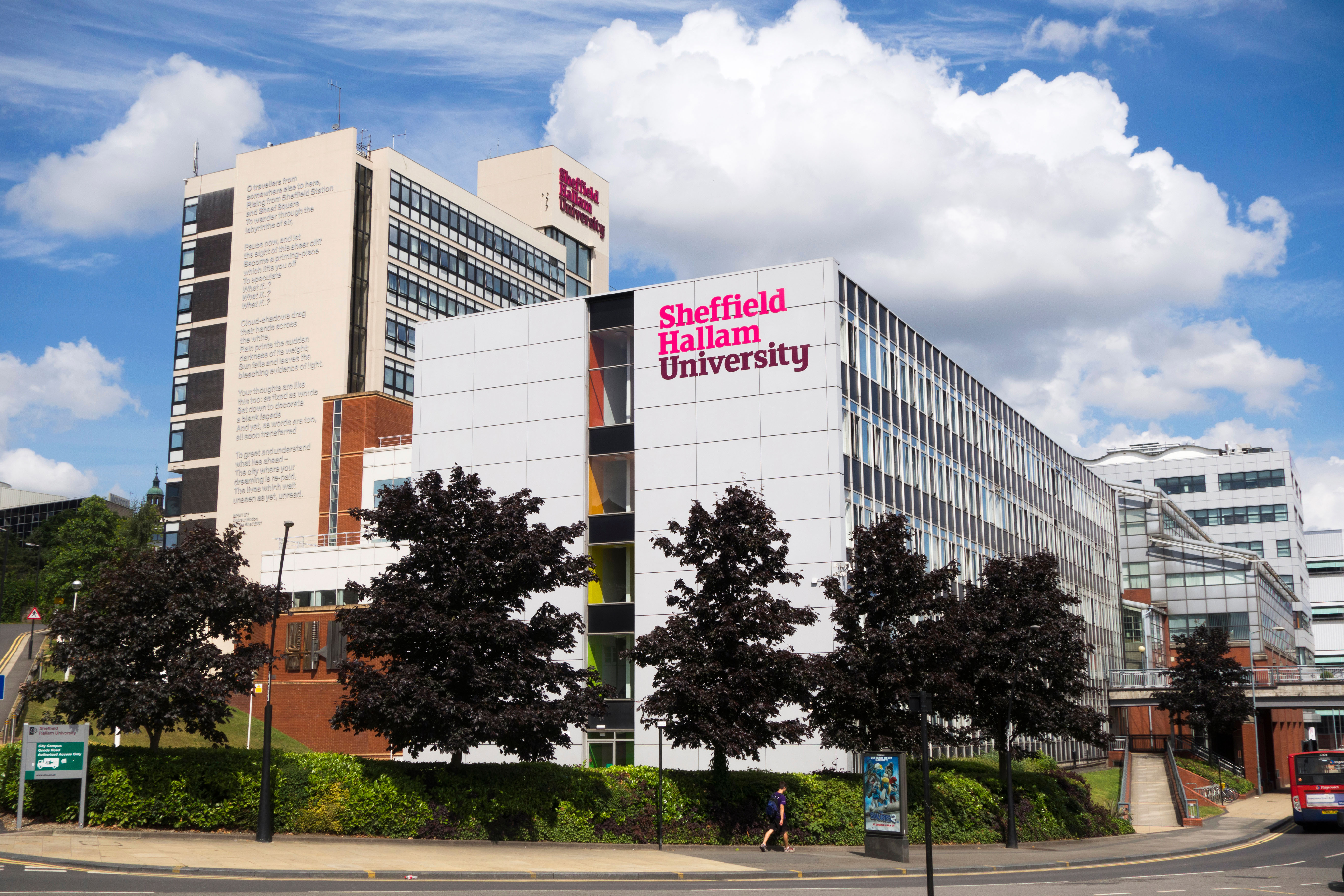 A modern building with "Sheffield Hallam University" signage on the facade reflects its commitment to excellence. Surrounded by trees, it features large, reflective windows and a tall, adjoining structure with text on its side—an inspiring setting for university admissions preparation under a partly cloudy sky.