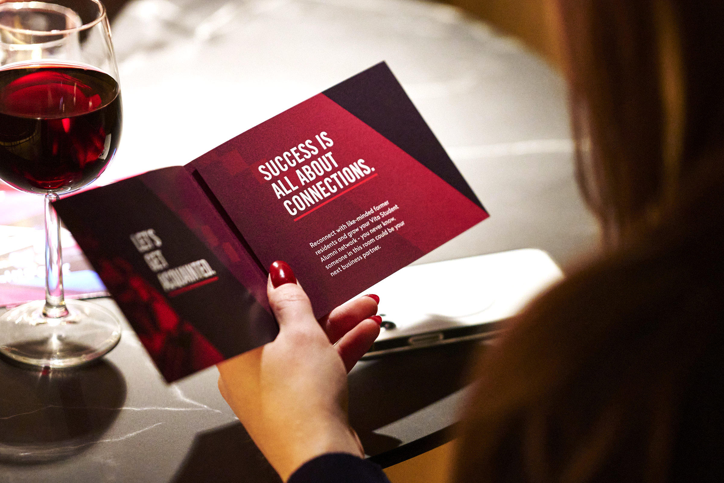 Person holding an open booklet with motivational text about connections. A glass of red wine is on the table beside them, and a phone is visible in the background.
