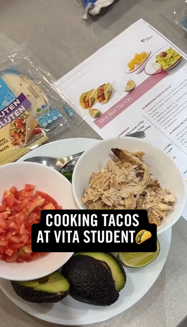 Top view of a kitchen counter with ingredients for tacos, including gluten-free wraps, chopped tomatoes, shredded chicken, avocado, and lime. There is also a recipe and a caption reading, "COOKING TACOS AT VITA STUDENT," with a taco emoji.