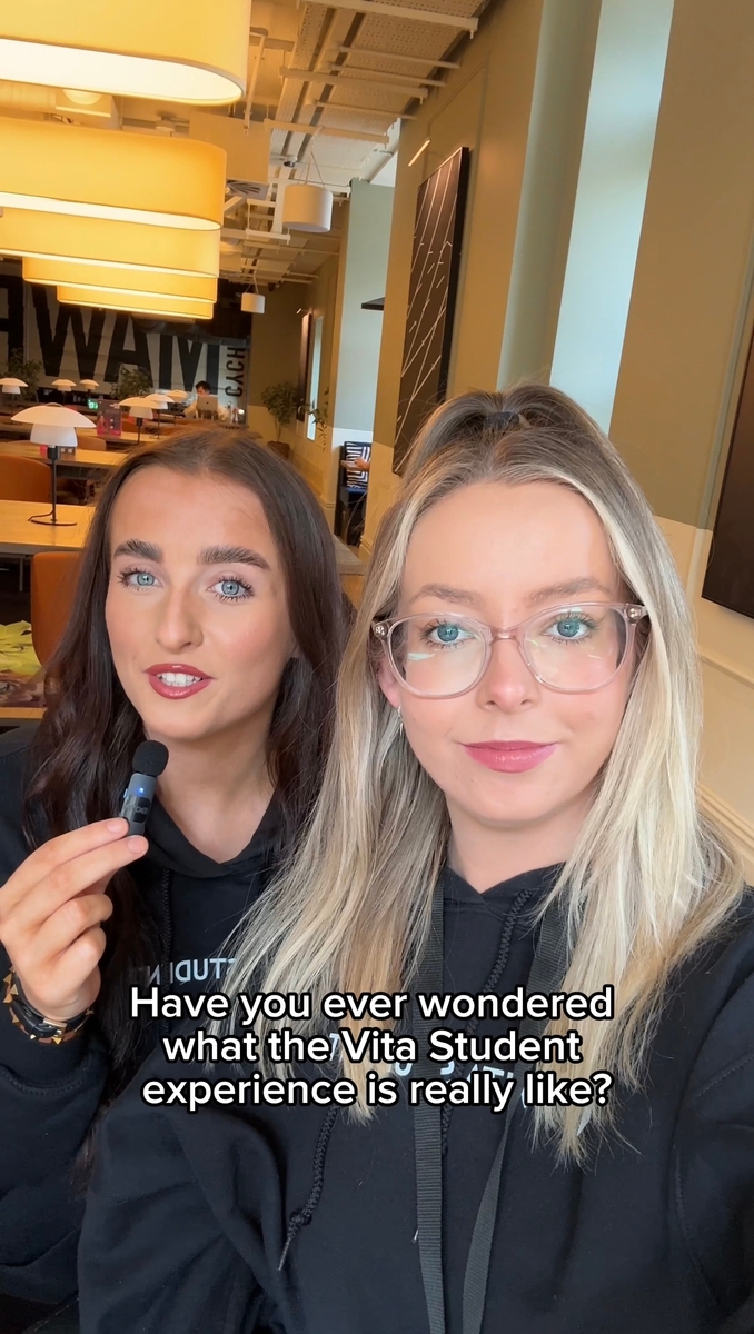 Two women are in a modern, well-lit lounge, with one holding a small object. Both are wearing black tops, and a caption reads, "Have you ever wondered what the Vita Student experience is really like?.