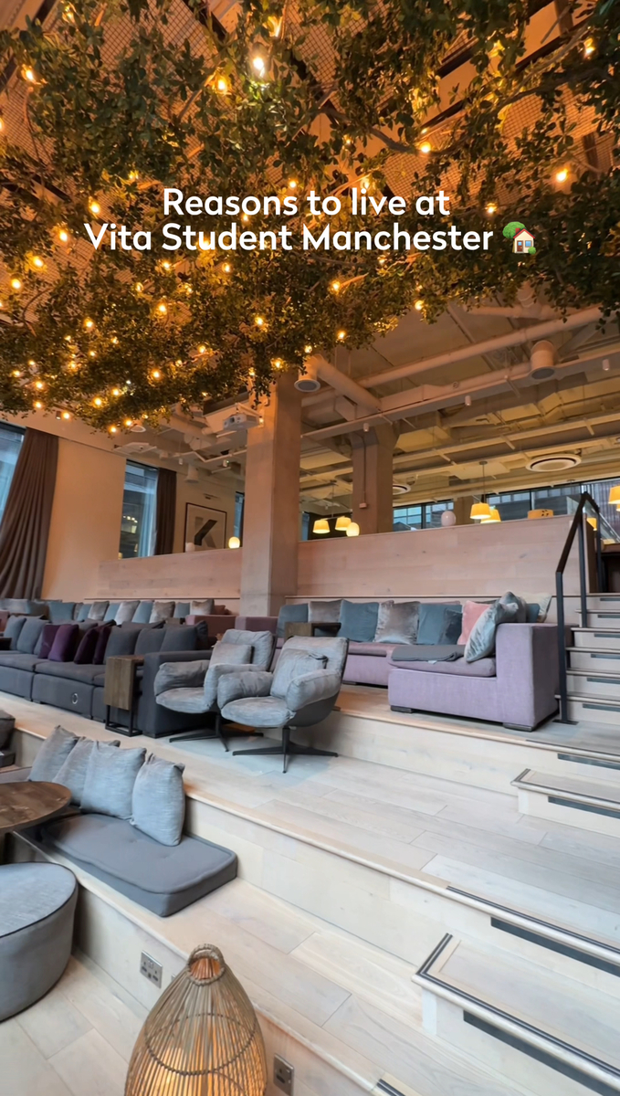 A modern, cozy seating area in a student housing complex with layered seating, cushions, and a lush, plant-covered ceiling. Warm lighting creates an inviting atmosphere. Text overlays at the top read: “Reasons to live at Vita Student Manchester.”.
