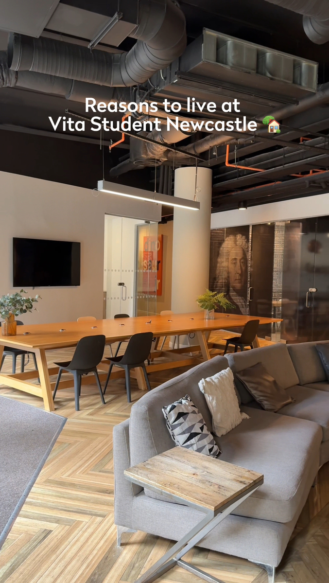 Contemporary lounge with a large wooden table, black chairs, a gray sofa, and a geometric cushion. Wall art and a TV adorn the walls. Text on the image reads "Reasons to live at Vita Student Newcastle.