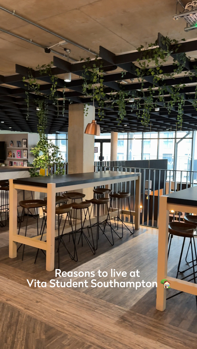 A modern, open-concept common area in Vita Student Southampton features high tables and stools. The ceiling is adorned with hanging plants, and the space is well-lit with large windows. Text reads "Reasons to live at Vita Student Southampton.