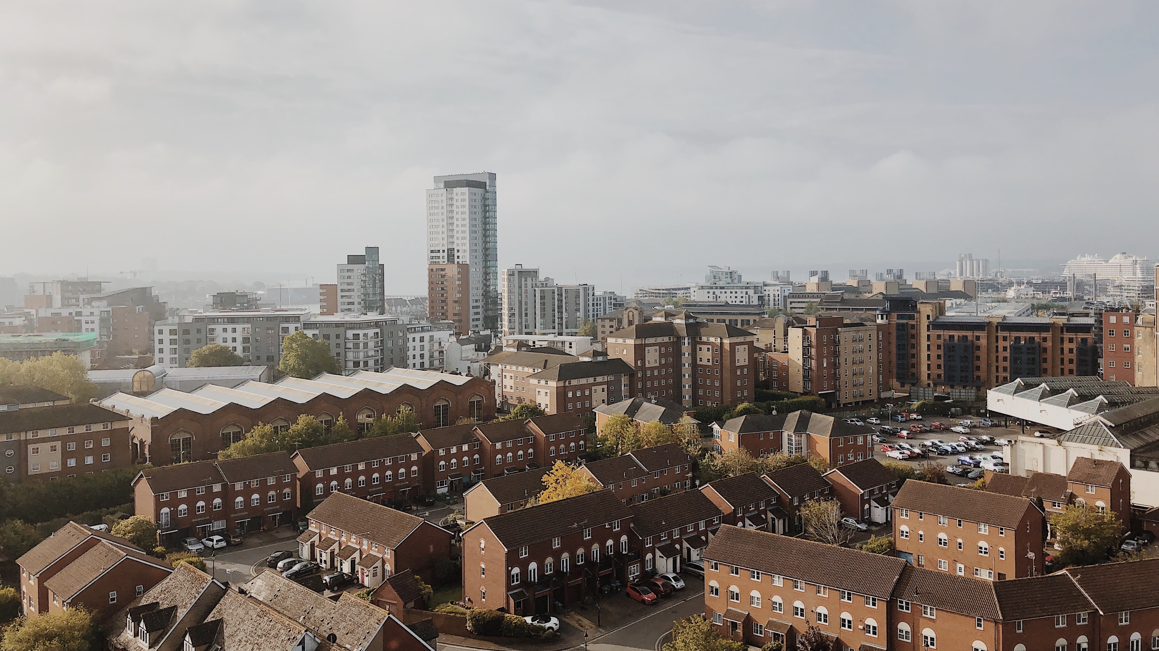 A cityscape of Southampton featuring rows of red-brick houses in the foreground and modern high-rises behind, under a cloudy sky. Parked cars dot the scene, highlighting a great place to live and study.
