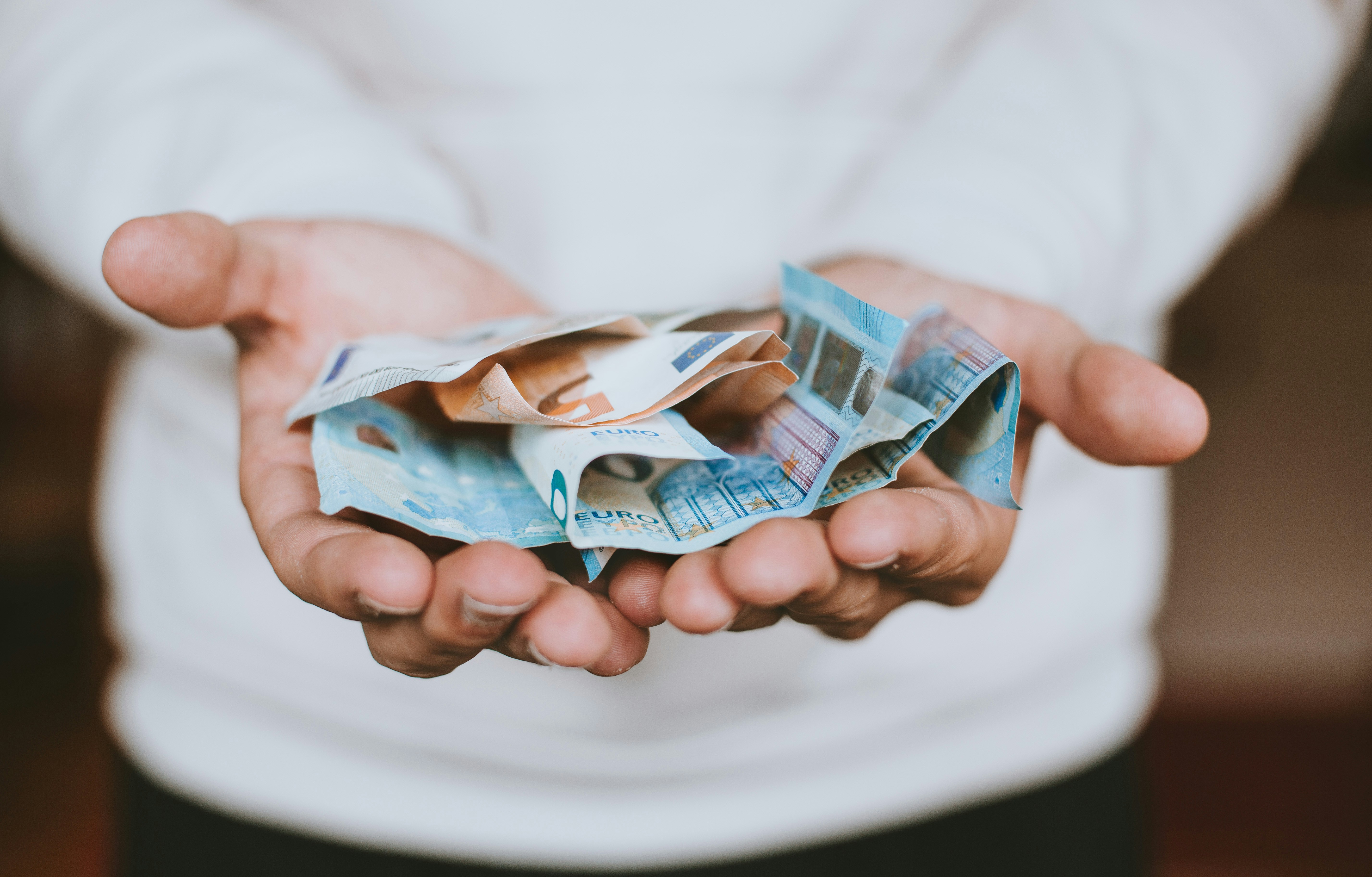 A person wearing a white shirt holds several crumpled euro banknotes in their outstretched hands, reflecting the challenges of finanzas estudiantes internacionales and the struggle to maximize ahorro estudiantes.