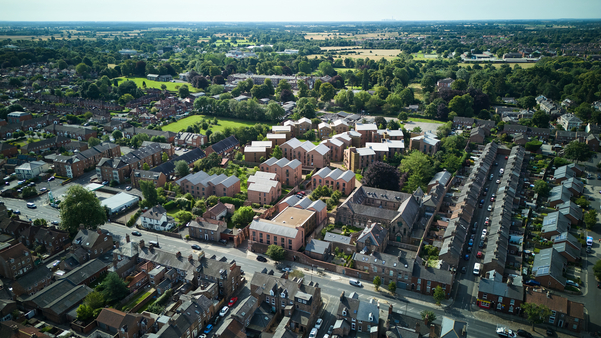 Aerial view of a suburban neighborhood in York, ideal for international student living, with rows of houses, green trees, and open fields under a clear sky. The scene captures residential streets and a mix of older and newer buildings—a perfect place to live.