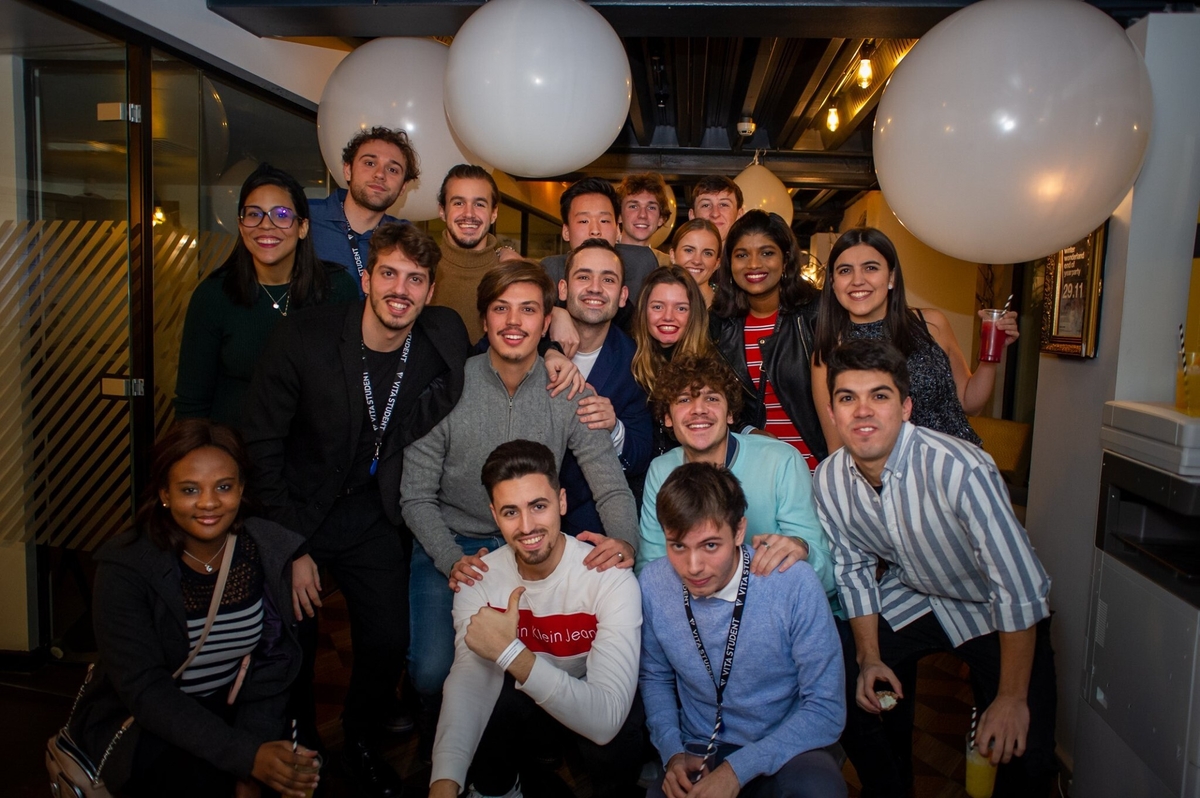 A group of young adults poses and smiles for a photo at a friendly, festive Vita Student event. Large white balloons decorate the indoor student accommodation space, where everyone is dressed casually and enjoying the lively atmosphere.