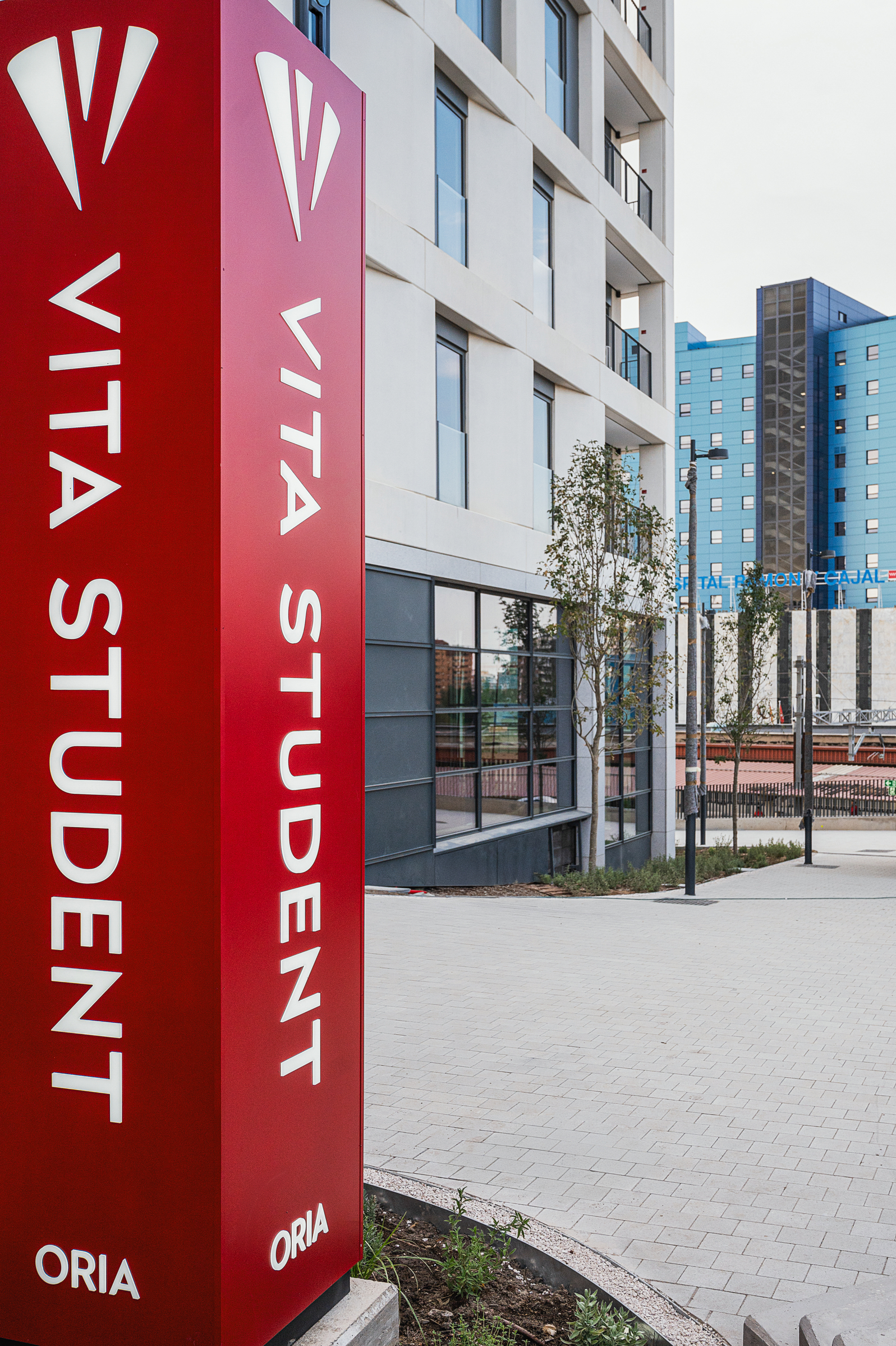A tall red sign reading “Vita Student” stands beside a modern apartment building, with another blue building visible in the background.