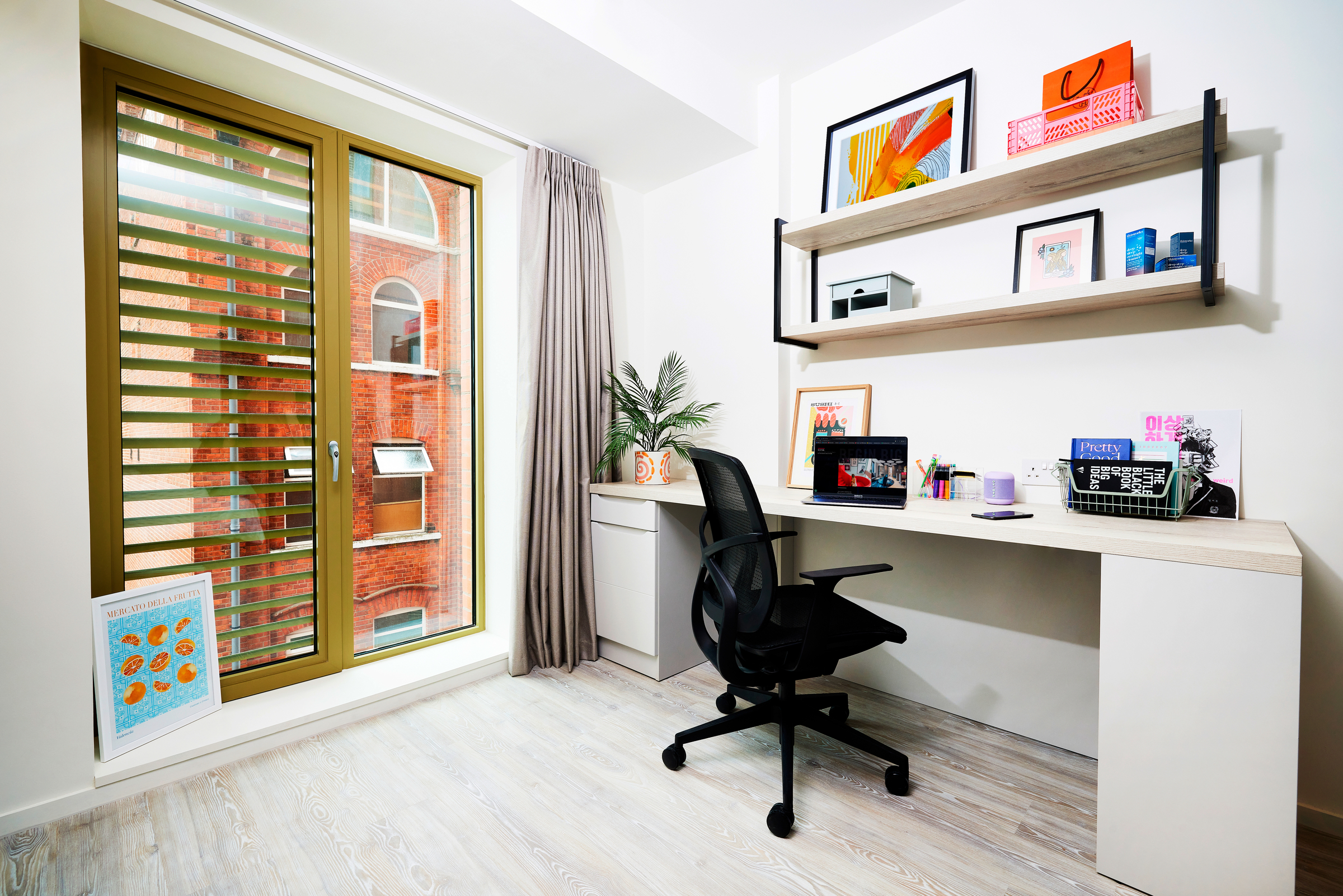 A modern, bright home office on Gough Street with a large window, desk, black chair, shelves filled with books and decor, framed art on the wall, a potted plant, and light wood flooring.