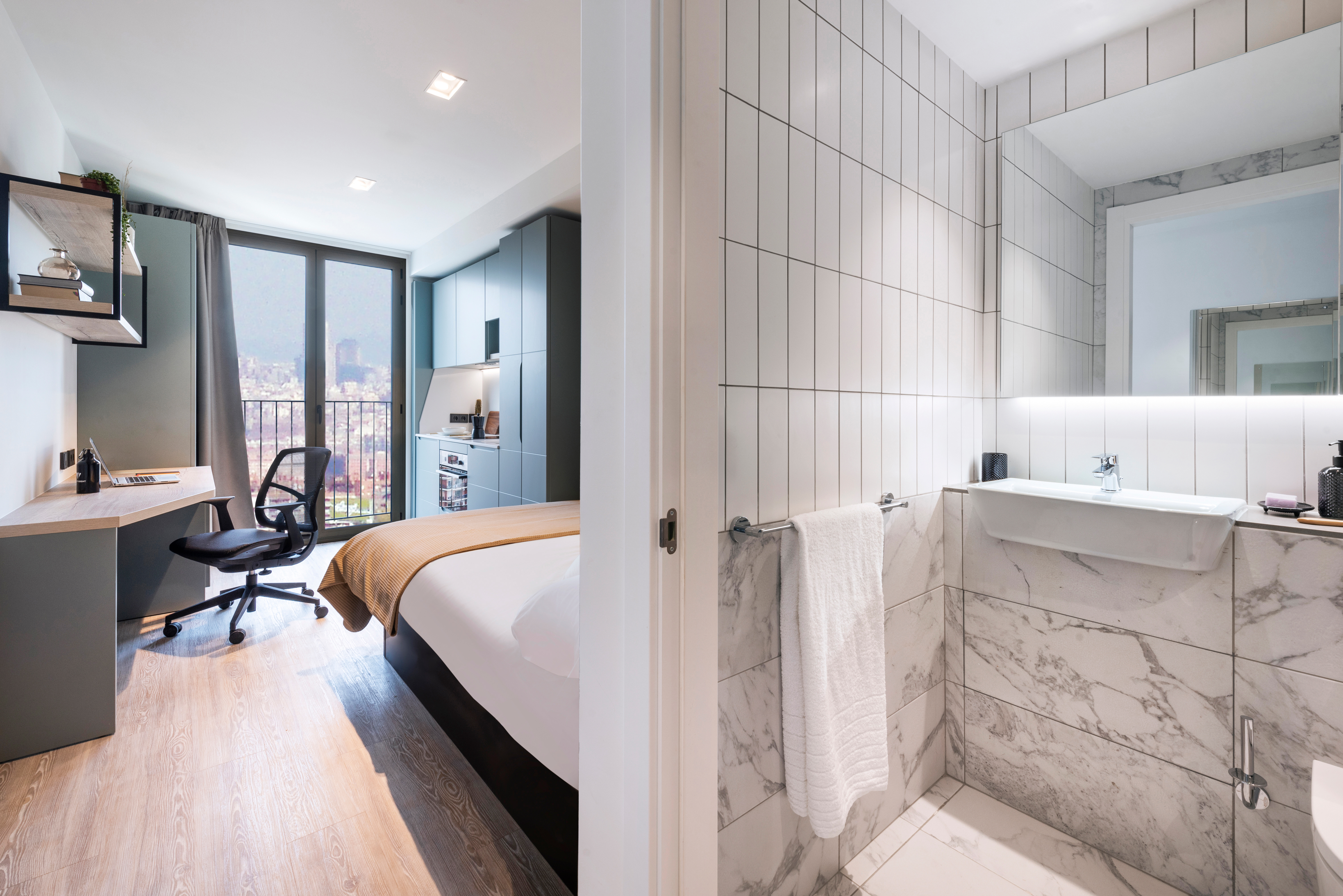 A modern apartment split view shows a bedroom with a desk, chair, bed, and large window on the left, and a bright bathroom with tiled walls, a sink, and towel on the right.
