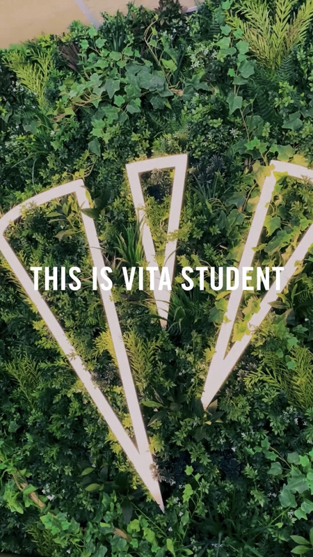 A green wall covered in lush plants with large white geometric shapes and the text "THIS IS VITA STUDENT" overlaid in bold white letters.