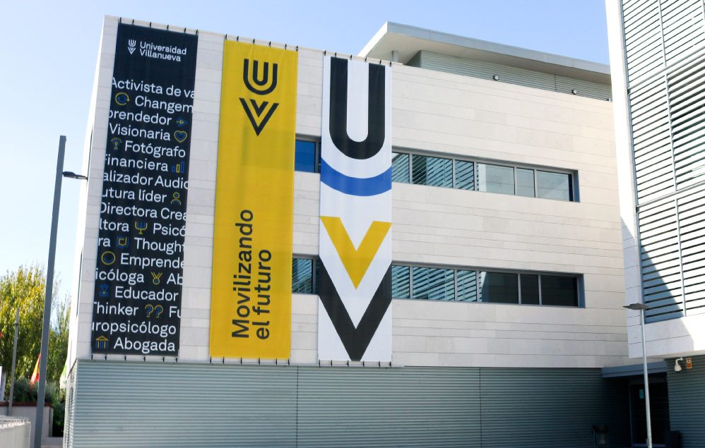 Modern building with large banners on the facade displaying the Universidad Villanueva logo and slogan “Movilizando el futuro.” Ideal for student accommodation in Madrid, it features white paneling and striking vertical windows.