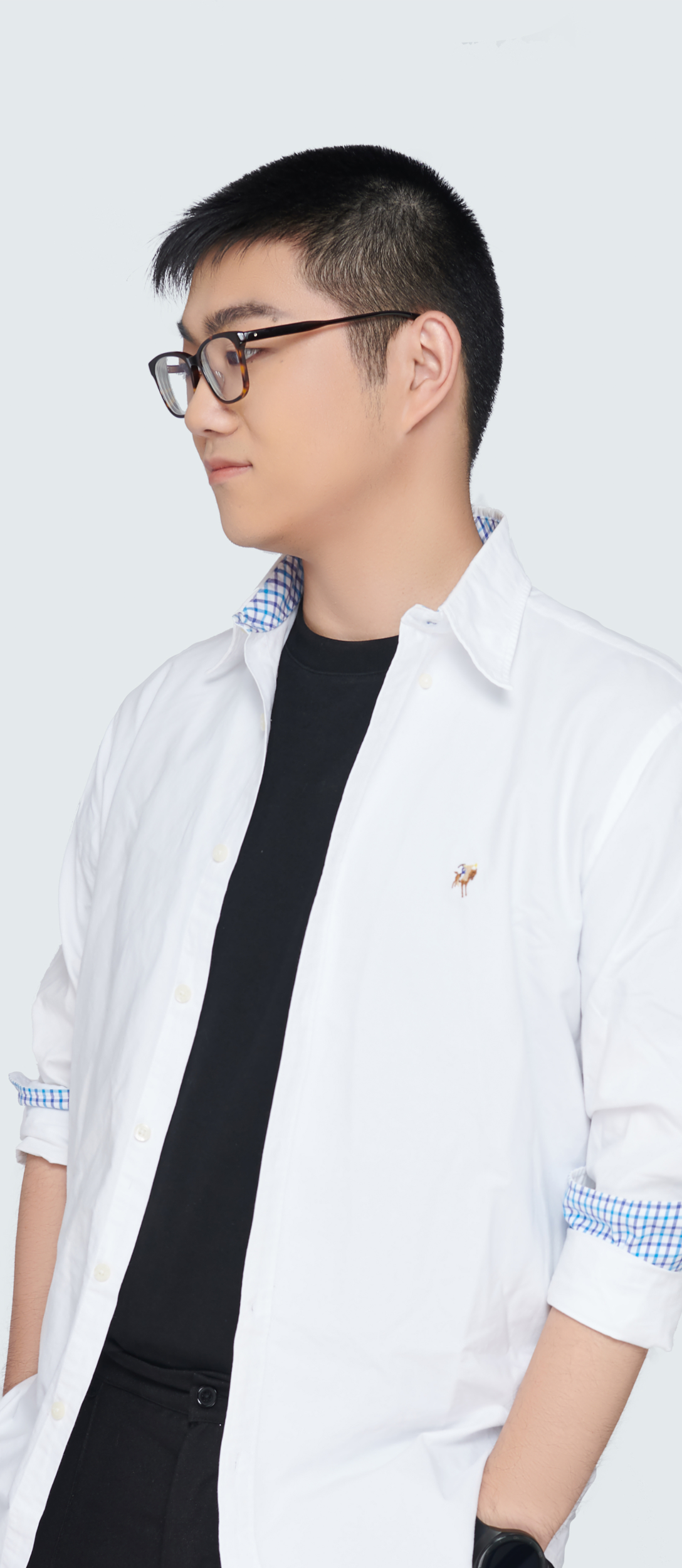 A young man with short black hair and glasses stands against a plain light background. Dressed in a white button-up over a black t-shirt, he looks to the side with his hands in his pockets, ready to take on new opportunities with his career tools.
