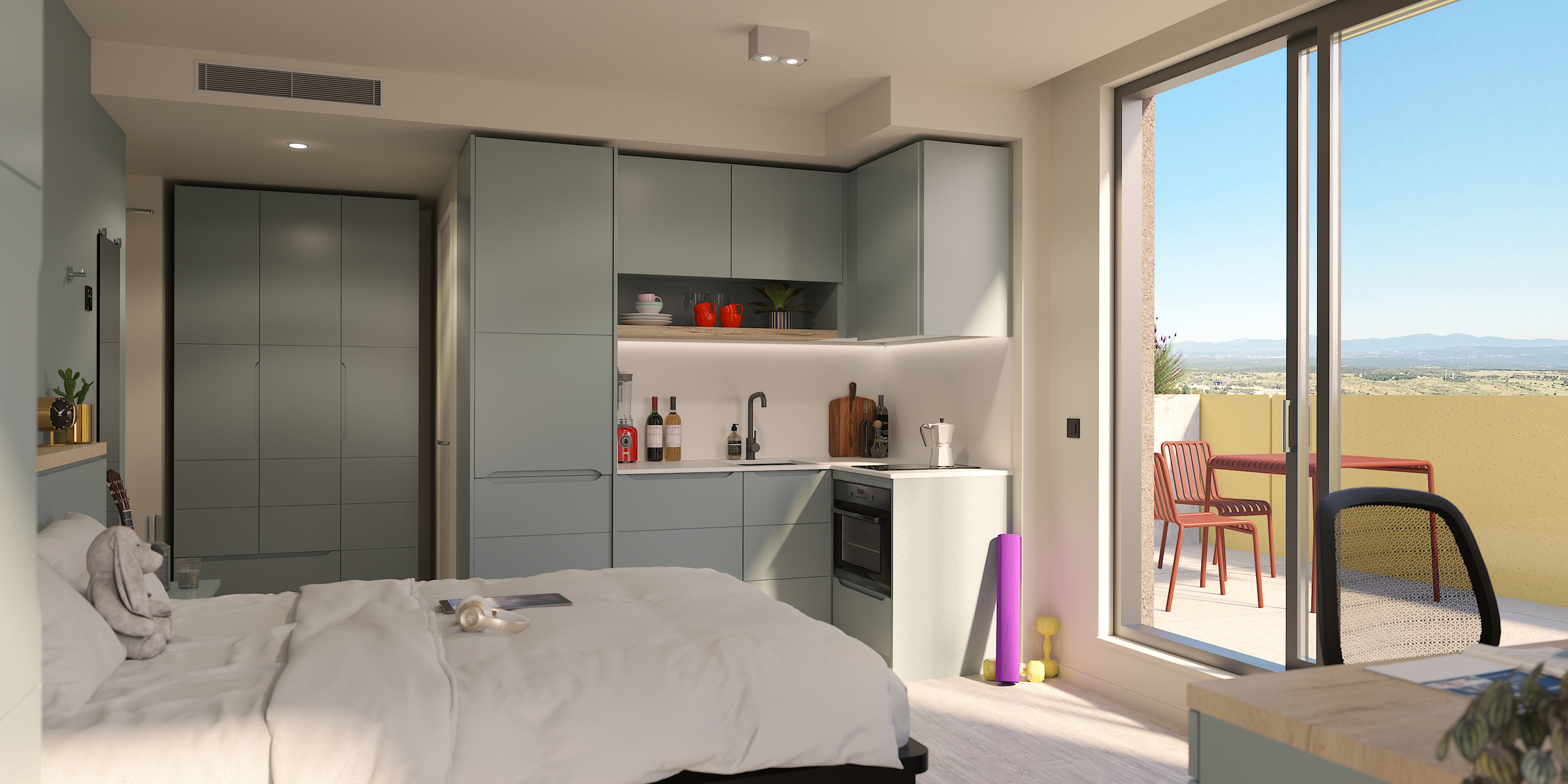 A modern studio apartment with a bed, kitchenette, and neatly arranged shelves. Large glass doors open to a balcony with a table, chairs, and a scenic outdoor view of mountains and fields.