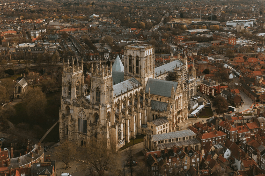 Aerial view of a large Gothic-style cathedral surrounded by densely packed red-roofed buildings and trees in York, with the historic cityscape offering unique study spots for University of York students.