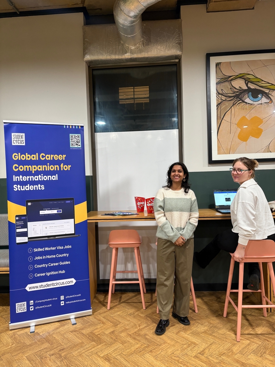 Two women stand and sit near a high table in a modern room. One works at her laptop as they smile together. A blue banner about global careers for international students and tips on CV Writing for UK Employers is displayed to the left.