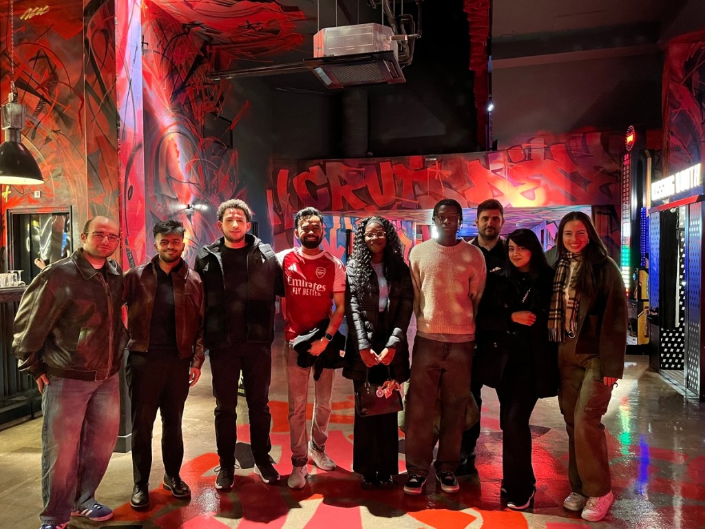 A group of nine people, including Vita Student residents, stand side by side, smiling for a photo in a room with vivid red, black, and orange graffiti artwork. The dim lighting adds a warm, urban vibe—perfect for anyone pursuing a social media career.