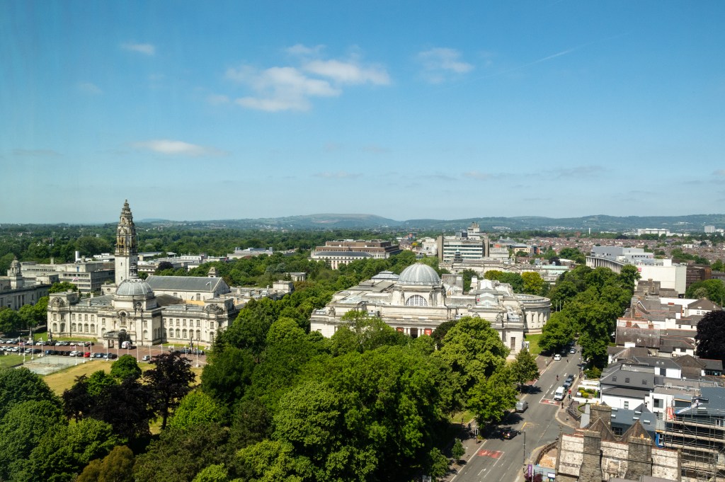 Aerial view of a cityscape with historic buildings and lush trees under a clear sky, featuring a prominent clock tower and distant hills—perfect for discovering things to do in Cathays or popular Cathays activities enjoyed by students.