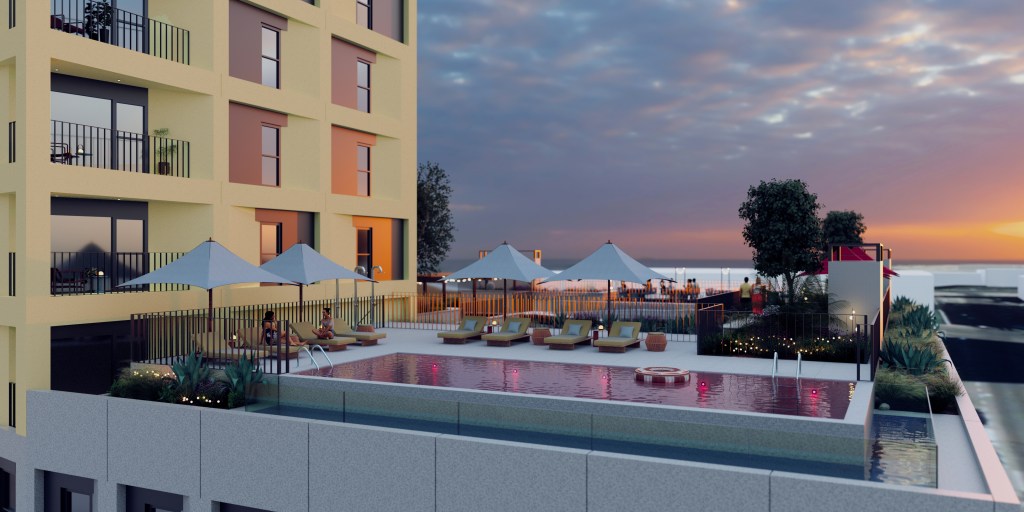 A modern Madrid student accommodation building with balconies overlooks a rooftop pool surrounded by lounge chairs, umbrellas, and decorative plants. The sun sets over the ocean in the background, creating a serene atmosphere.
