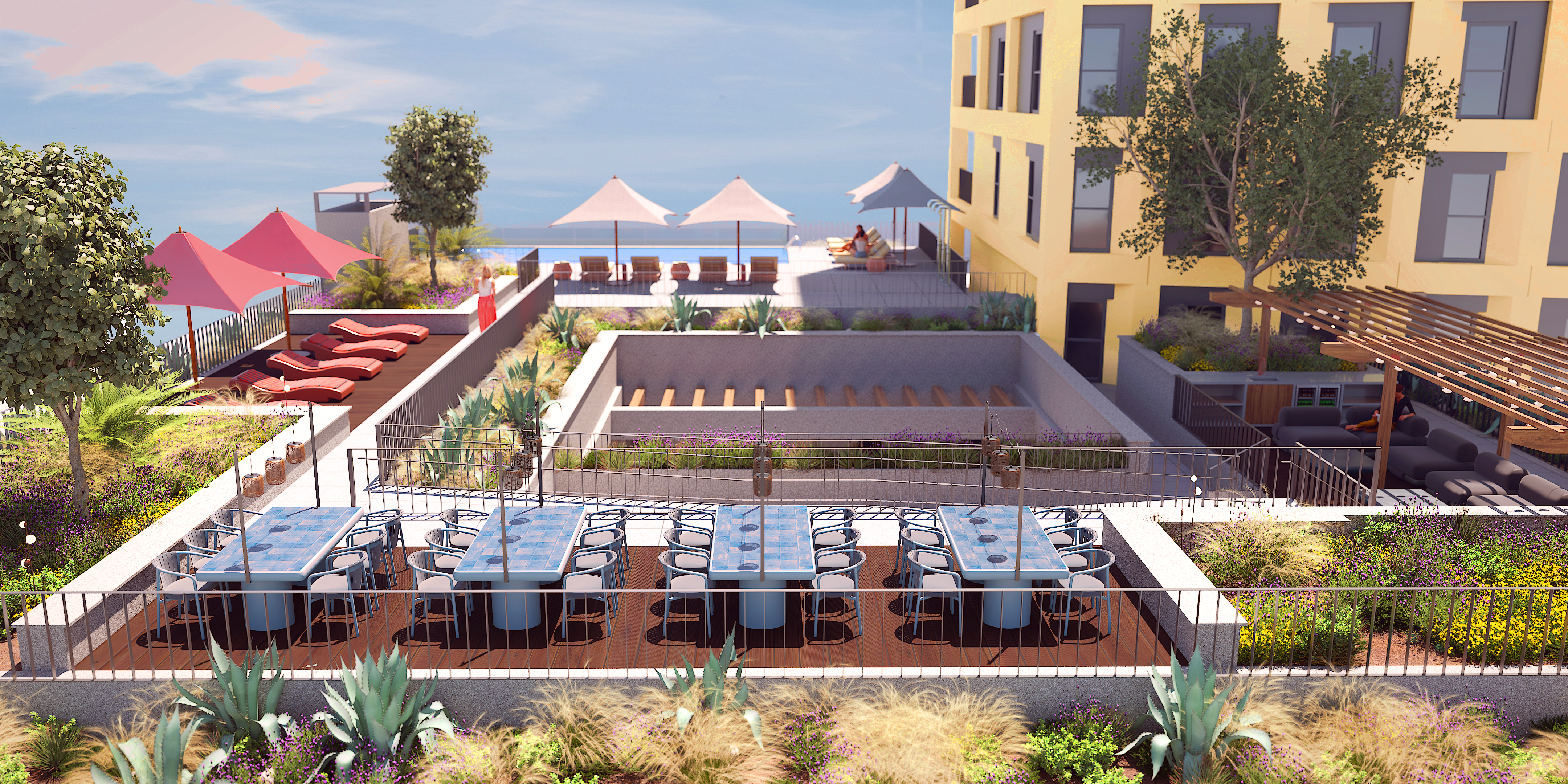 Rooftop terrace at a Madrid student accommodation with long dining tables, lounge chairs, shaded seating, lush landscaping, and ocean views. Enjoy modern outdoor furniture, vibrant plants, and a pergola near the inviting yellow building.