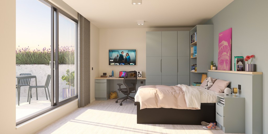 A modern, tidy bedroom in Madrid student accommodation featuring a large bed, built-in shelves, a desk with a computer, and glass doors opening to a patio with outdoor seating. The room is well-lit with natural light.