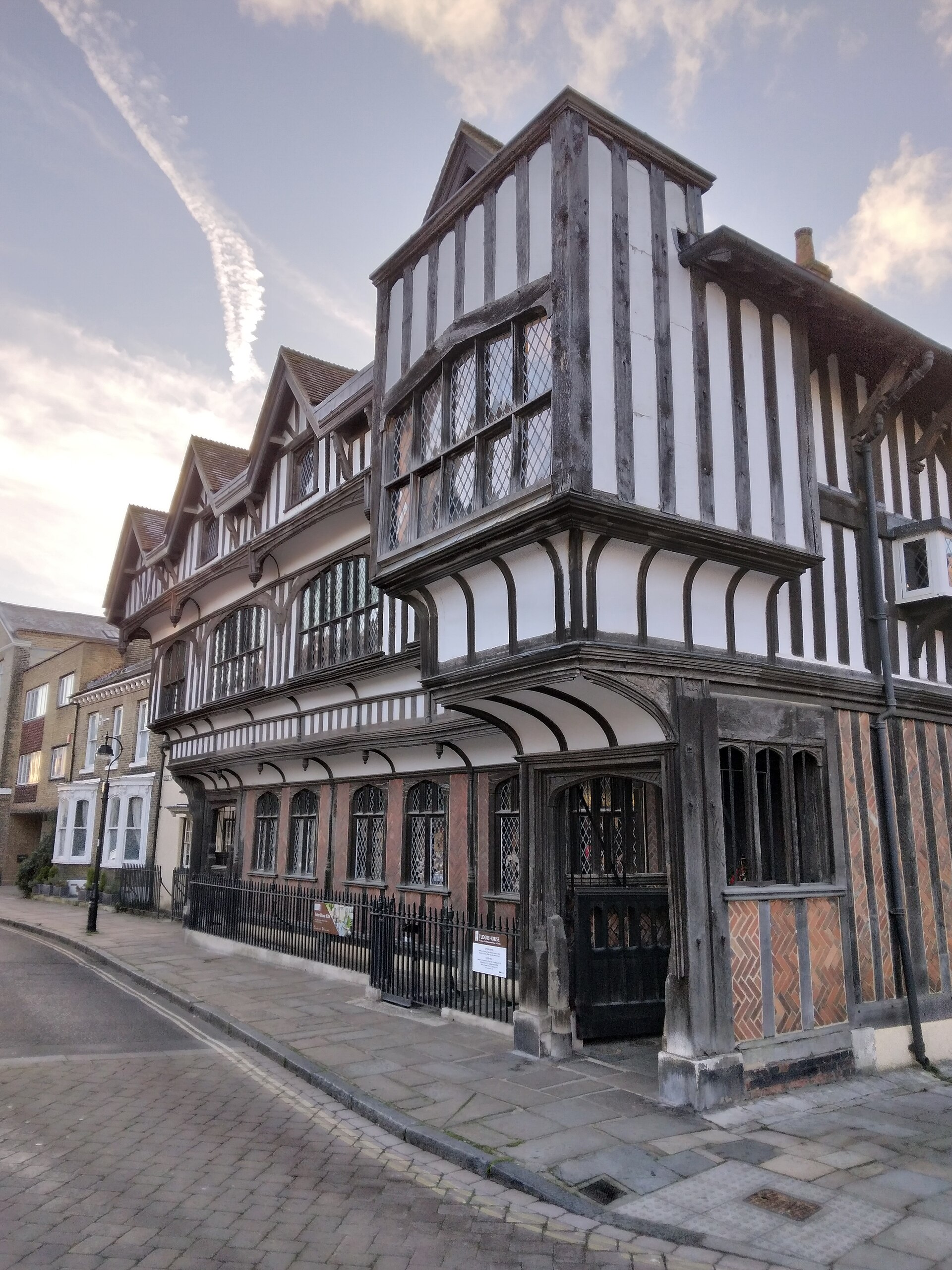 A historic timber-framed building in Southampton with black and white vertical wood and plaster panels, leaded glass windows, and overhanging upper floors, sits on a quiet city cobblestone street under a partly cloudy sky, often admired by students.