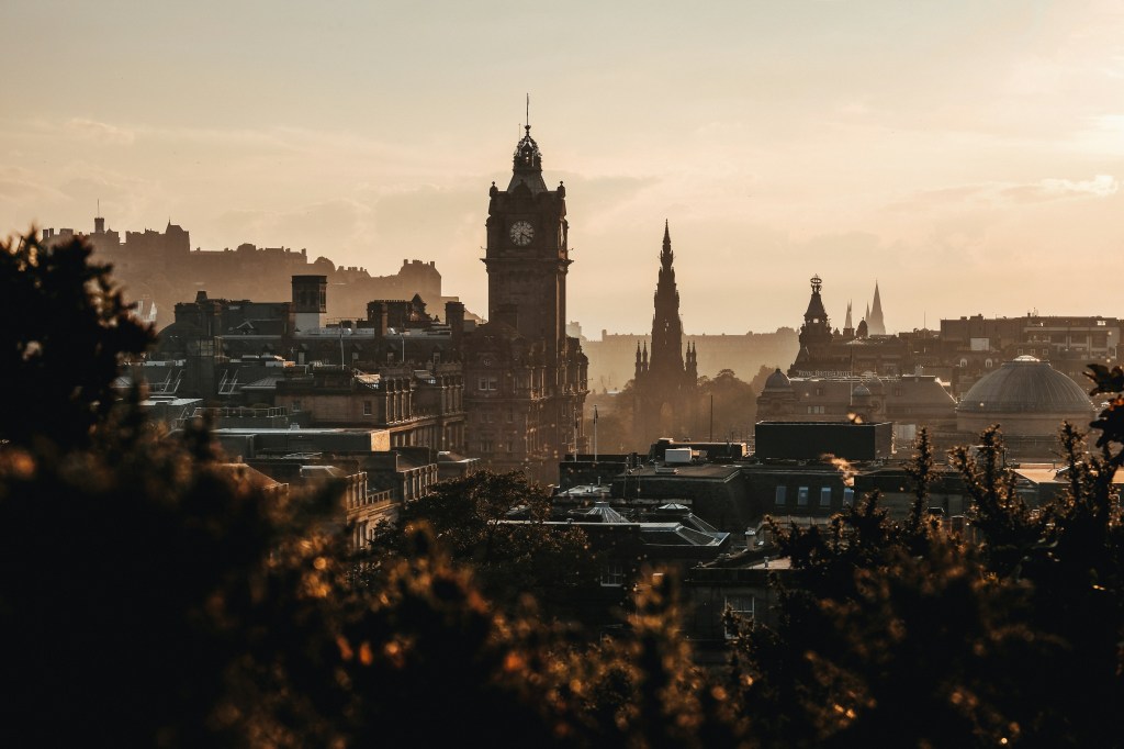 A cityscape of Edinburgh at sunset, featuring the Balmoral Hotel clock tower, the spire of the Scott Monument, and historic buildings bathed in soft golden light—perfect for students seeking things to do near New Waverley.