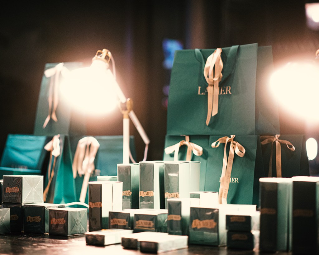 Gift bags and boxes of La Mer skincare products are arranged on a table under warm lighting, creating a luxurious touch to the Vita Student accommodation experience, with teal bags tied with cream ribbons in the background.