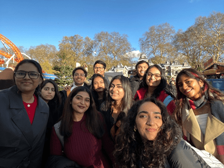 A group of young adults smiling and posing for a photo outdoors at an amusement park on a sunny day—capturing their leap of faith before riding the roller coaster, with trees and laughter in the background.