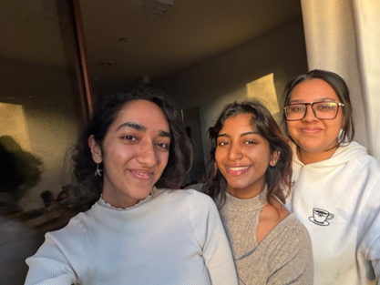 Three young women smiling and posing together indoors, warmly lit by sunlight coming through a window with curtains, celebrating their leap of faith after sharing inspiring student stories.
